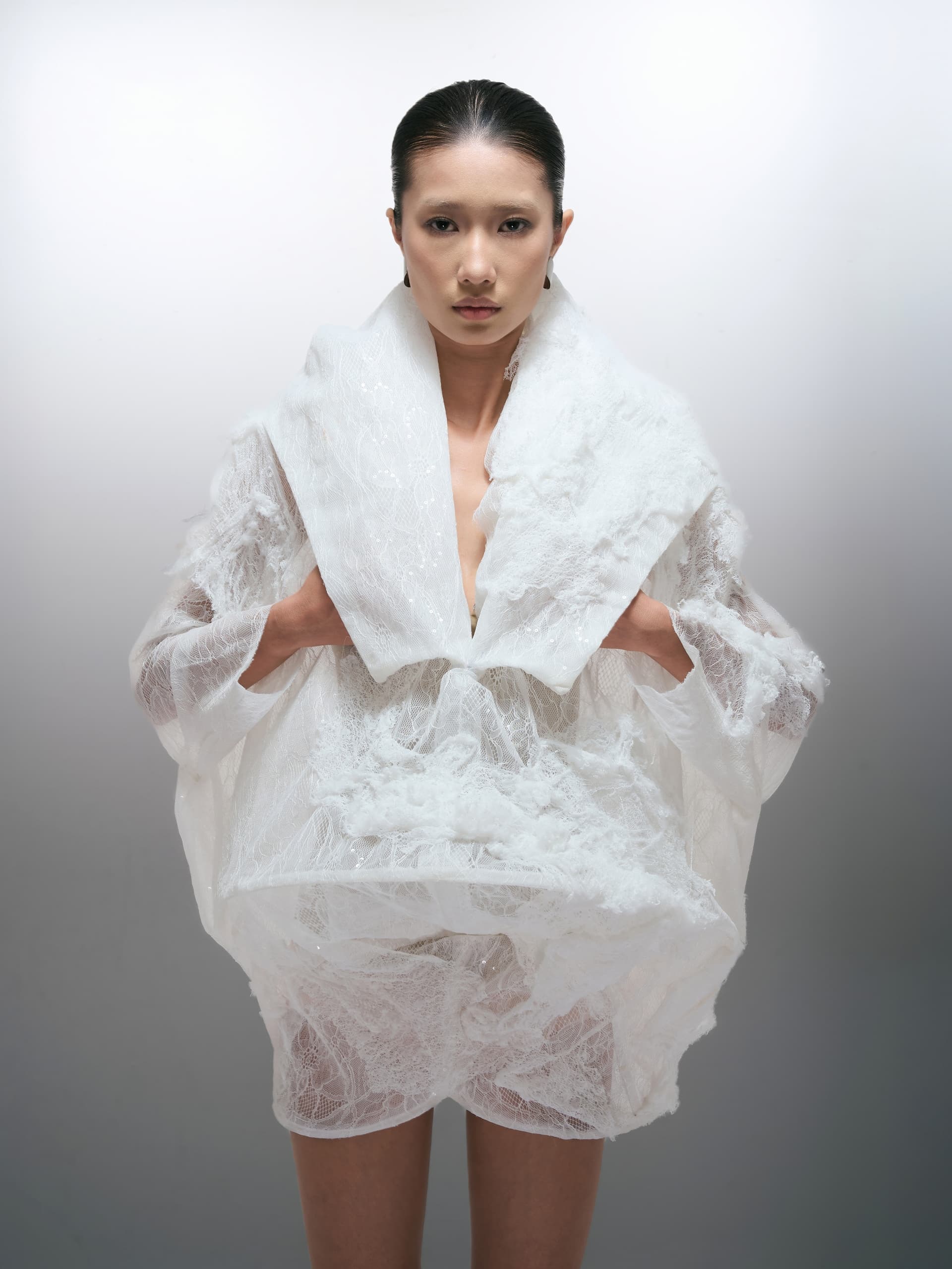 Fashion model in avant-garde white lace outfit against a neutral backdrop.