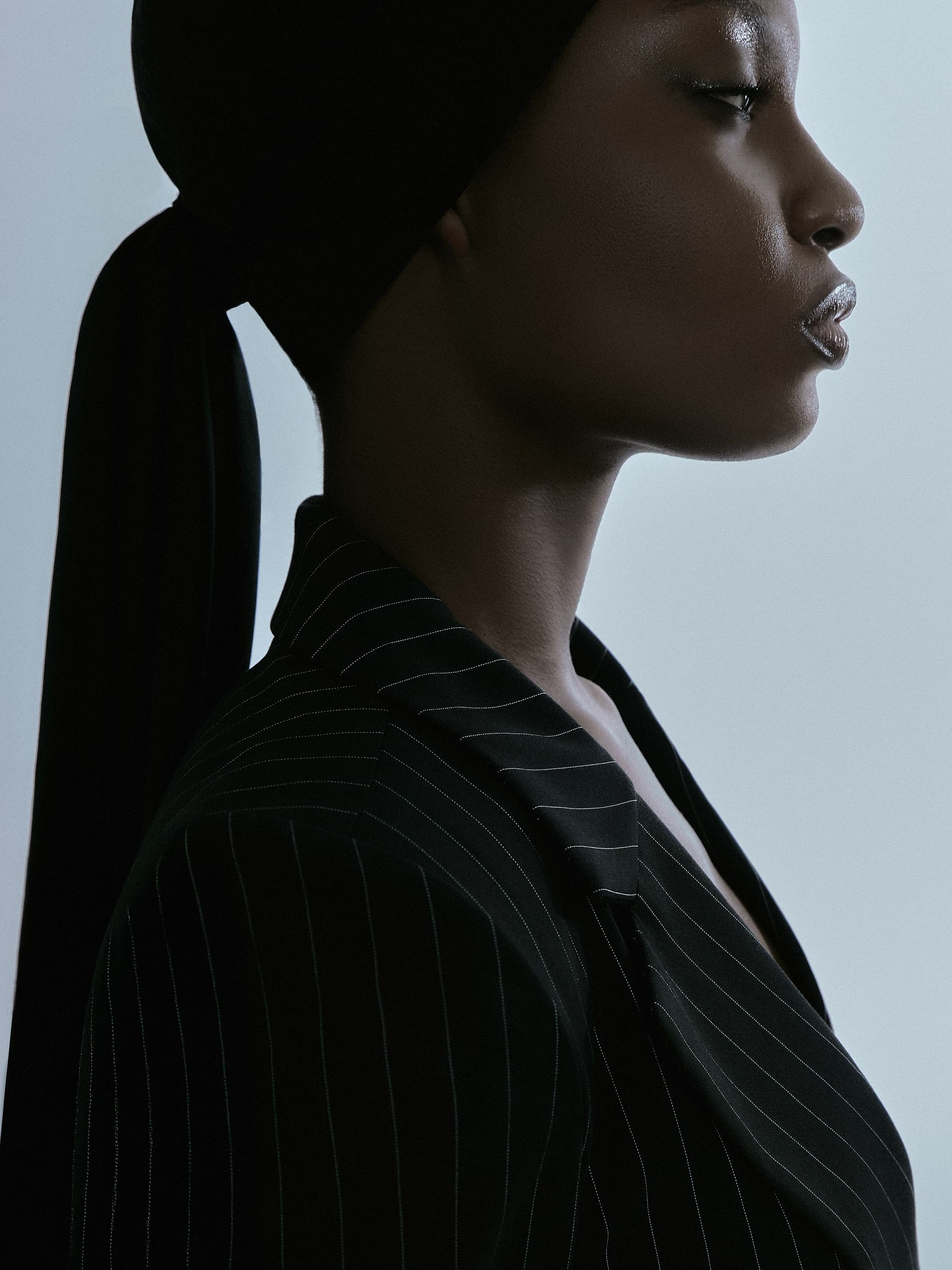 Profile view of a person in pinstripe suit and headscarf, elegant and poised.
