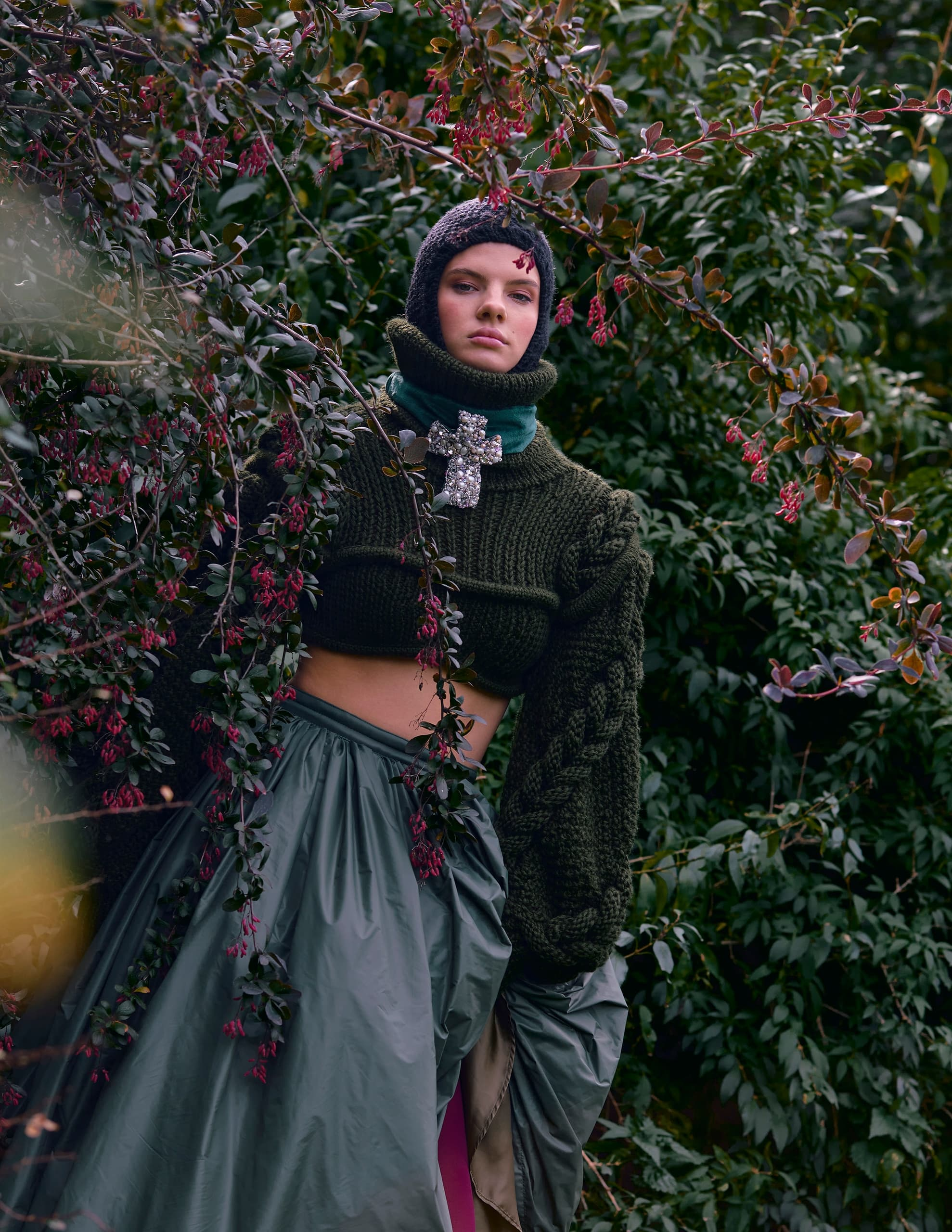 Fashionable woman in a garden wearing a green knitted outfit with sparkling brooch.