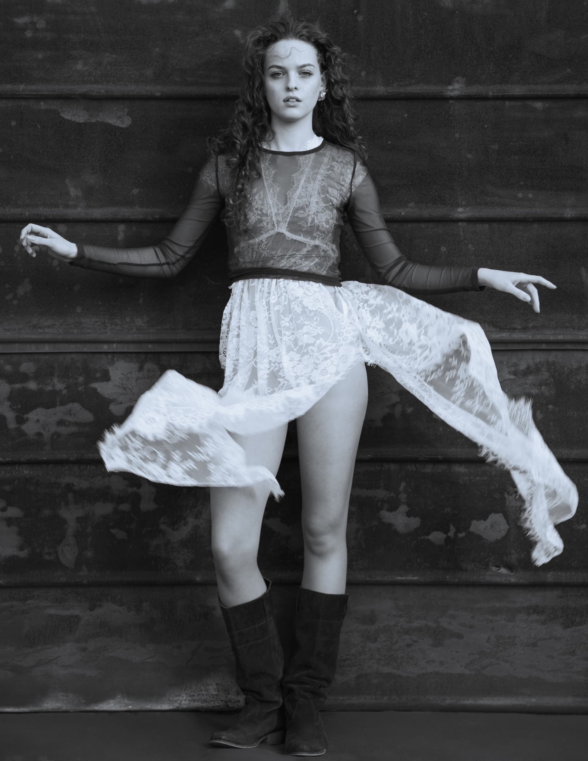 Model in lacy dress and boots against a textured wall. Monochrome image.