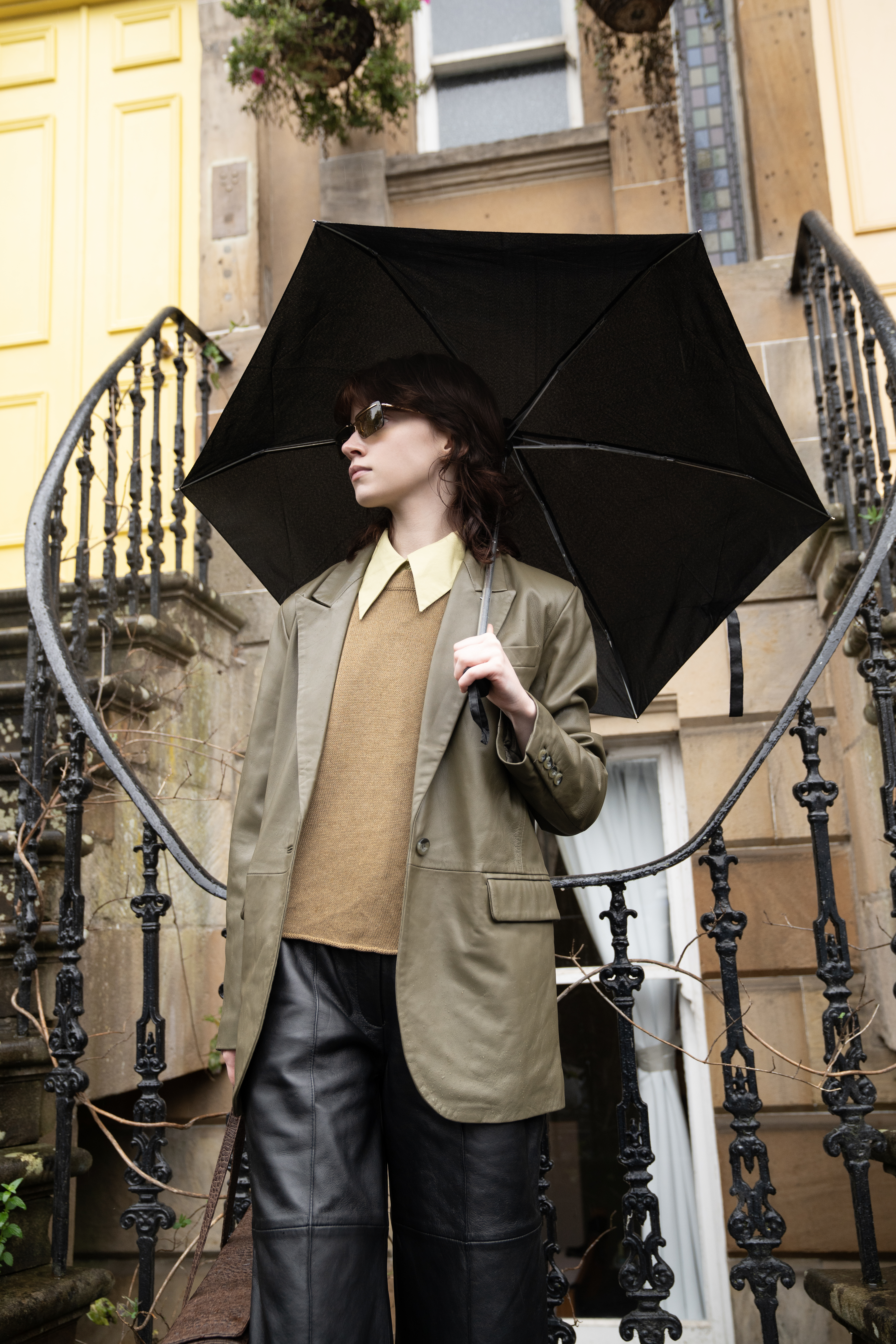 Person in stylish attire holds umbrella near vintage staircase.