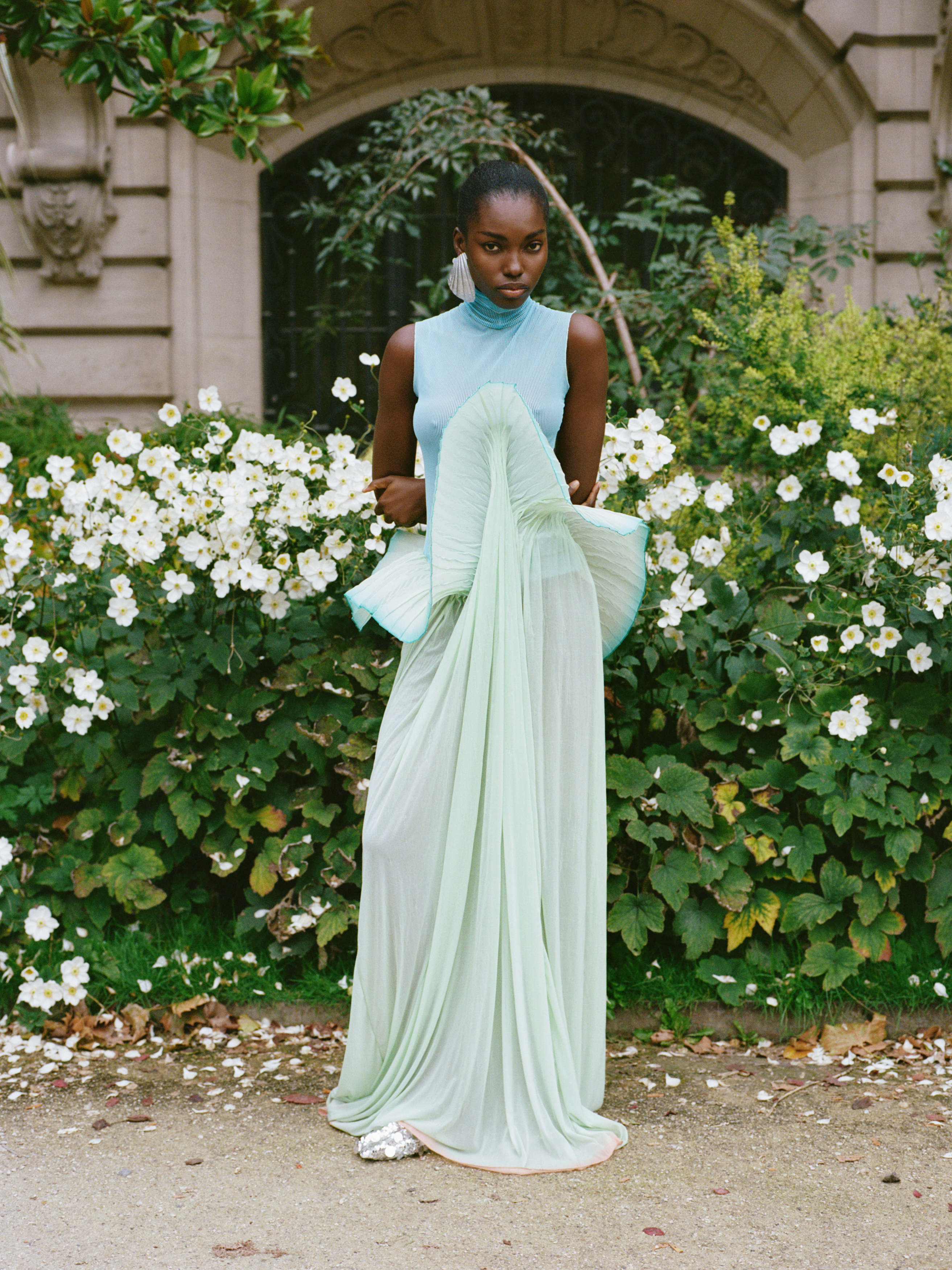 Elegant woman in flowing pastel dress amidst blooming garden flowers.