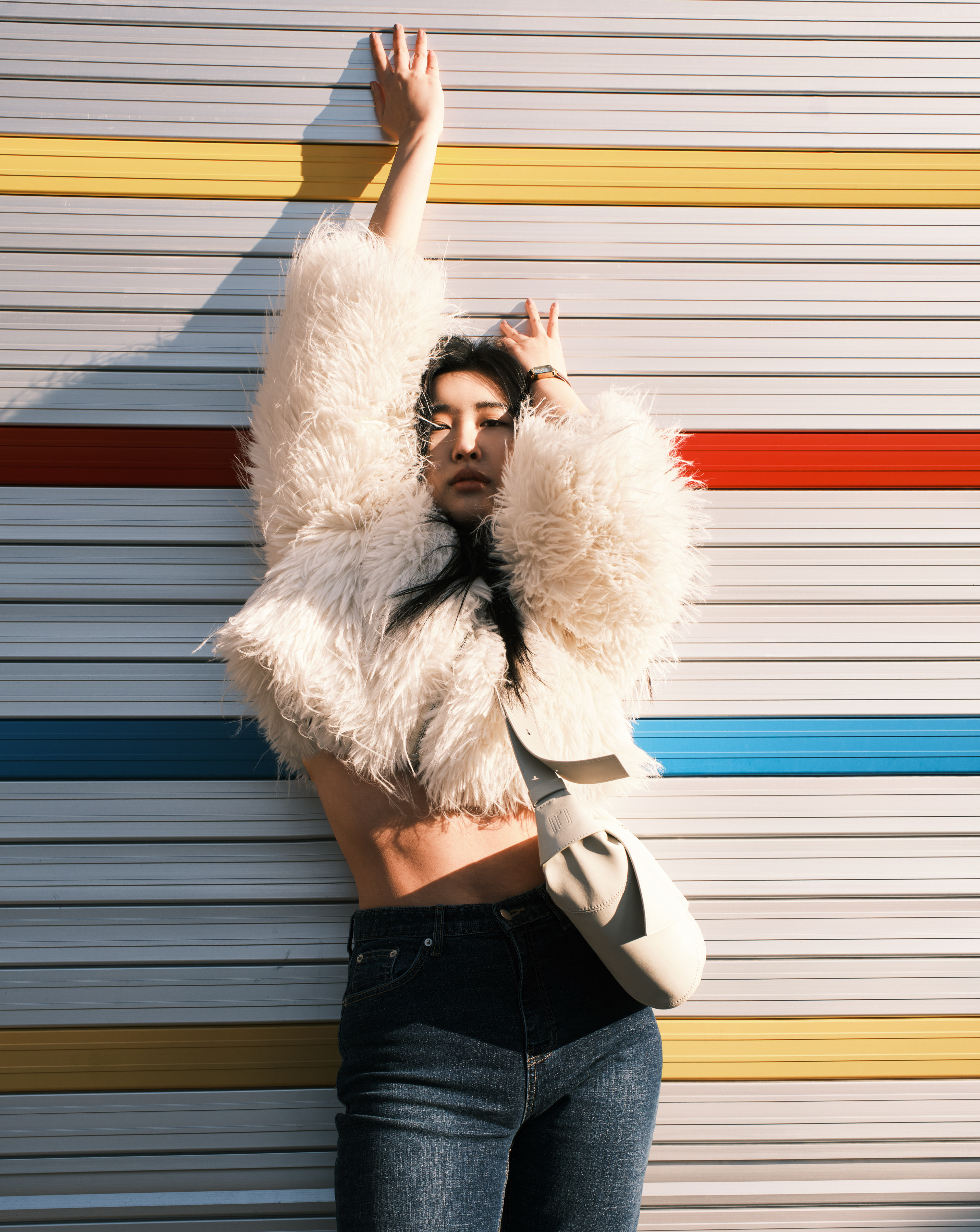 Fashionable person in a fluffy coat posing against a colorful striped background.