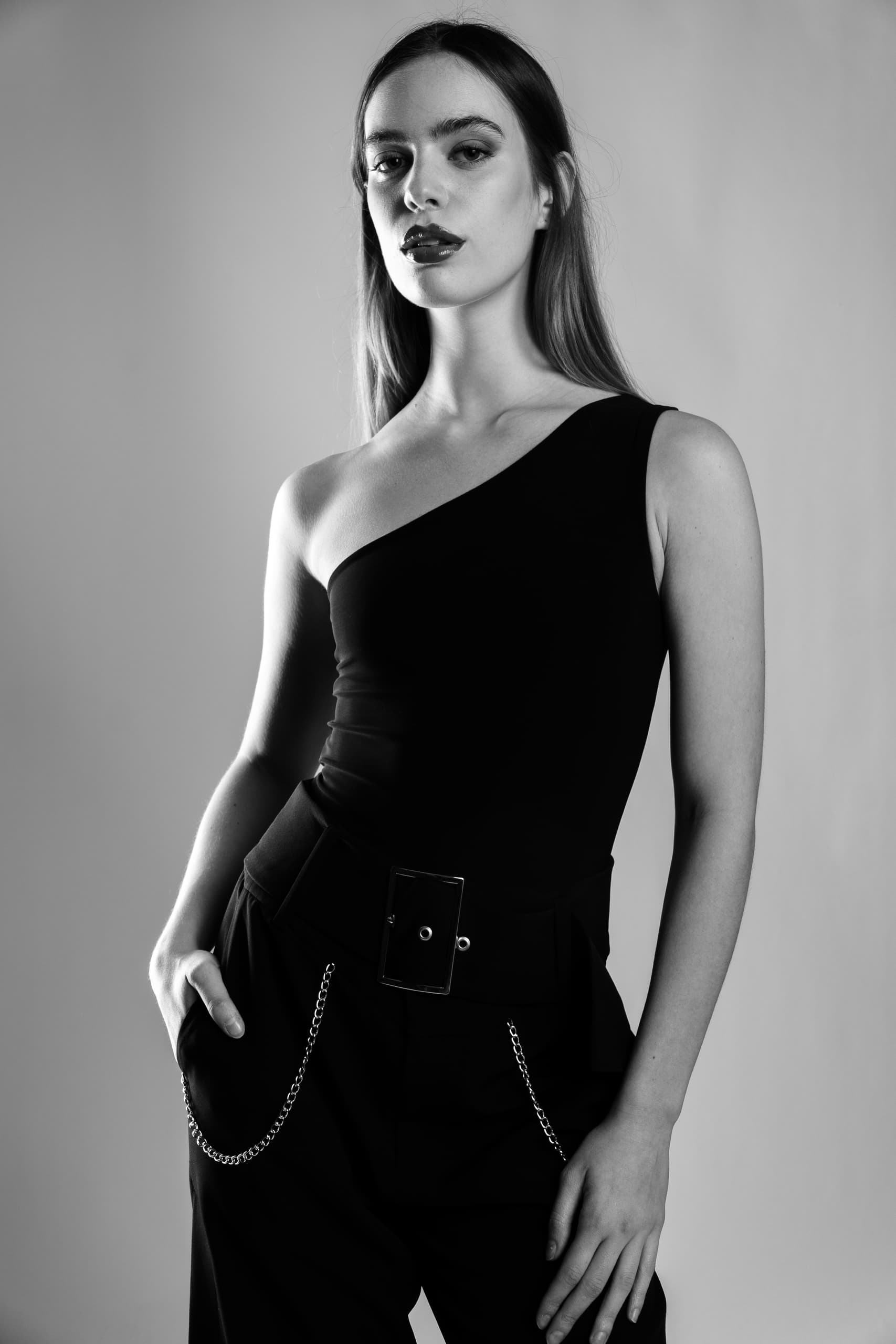 Black and white portrait of a model in a one-shoulder top with chain accents.