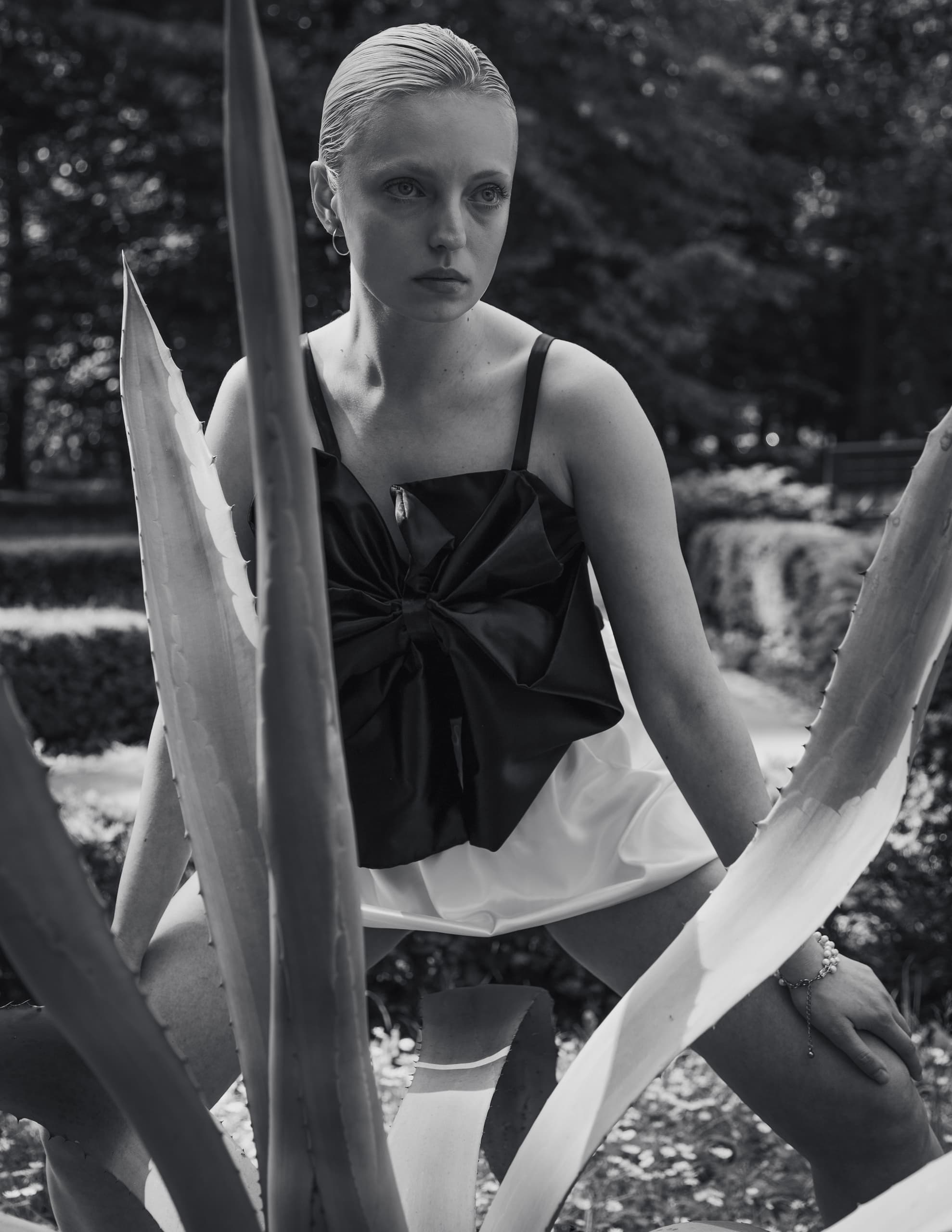 Black and white photo of a woman posing with spiky plants in a natural setting.