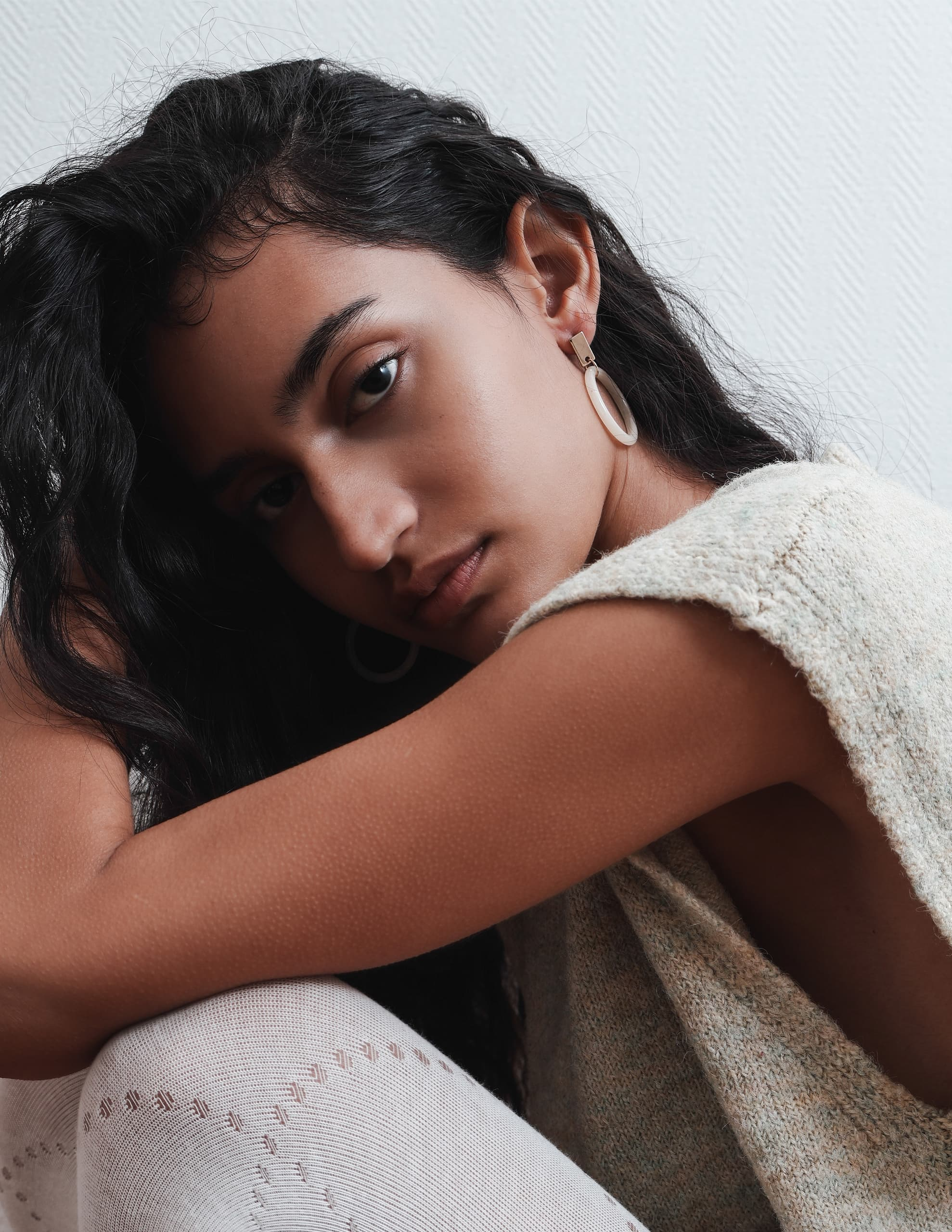 Woman with long hair wearing minimalist earrings, leaning on knees.