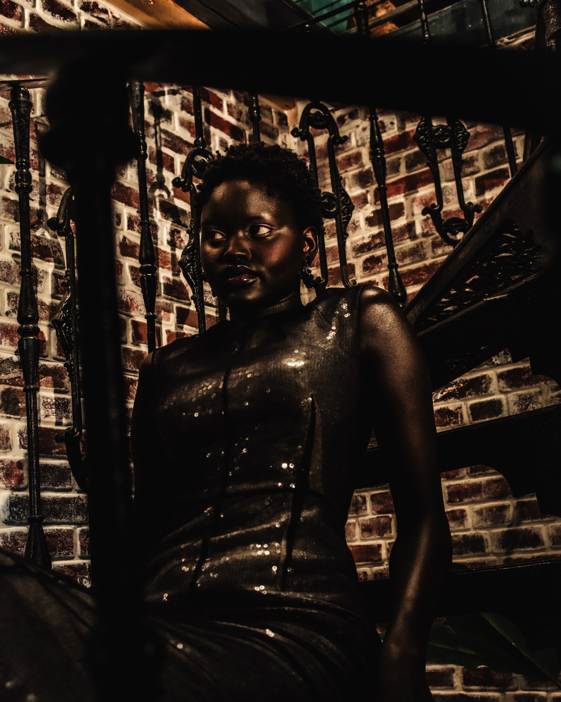 Person in a shimmering dress on a staircase with brick wall background.