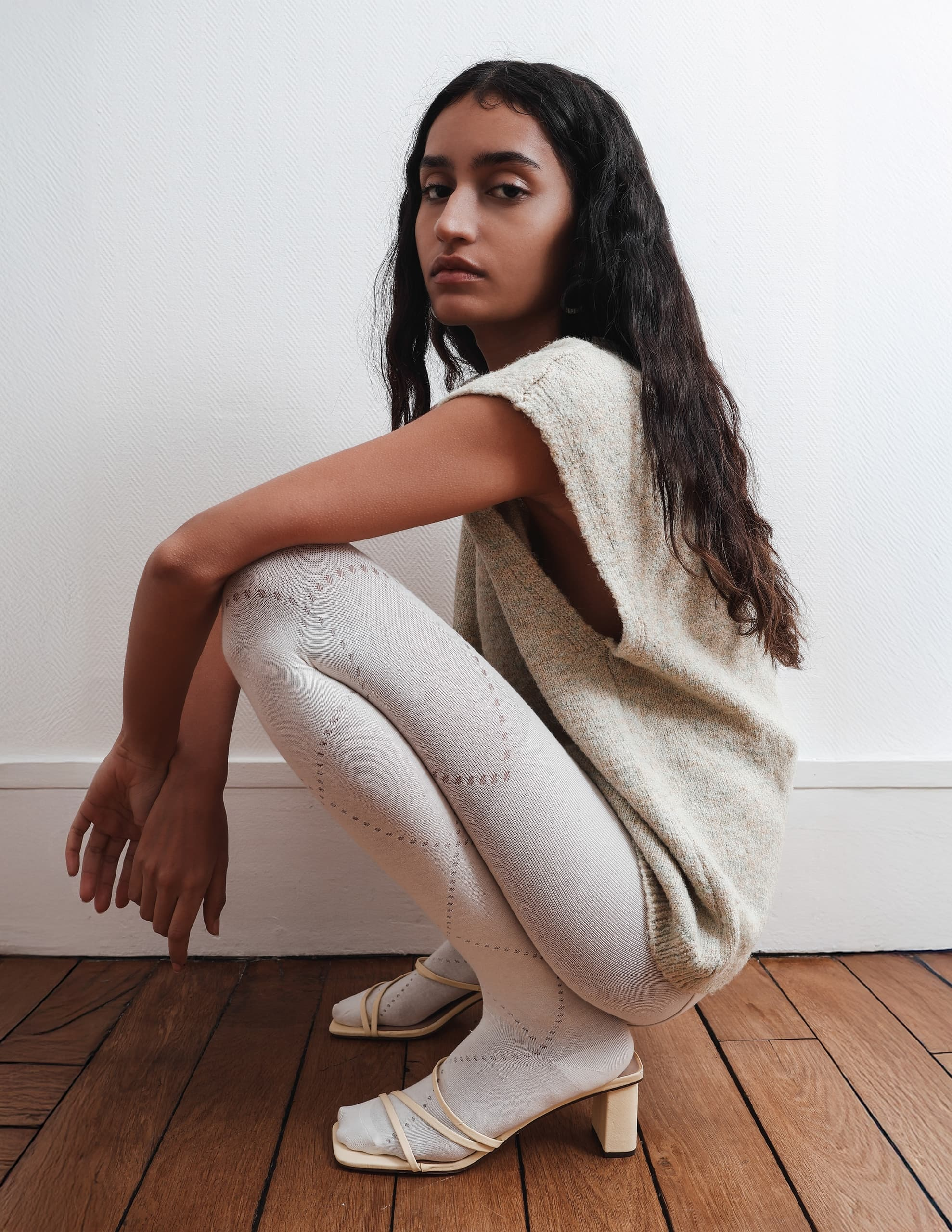 Fashion-forward woman in knitwear and tights, posing on a wooden floor.