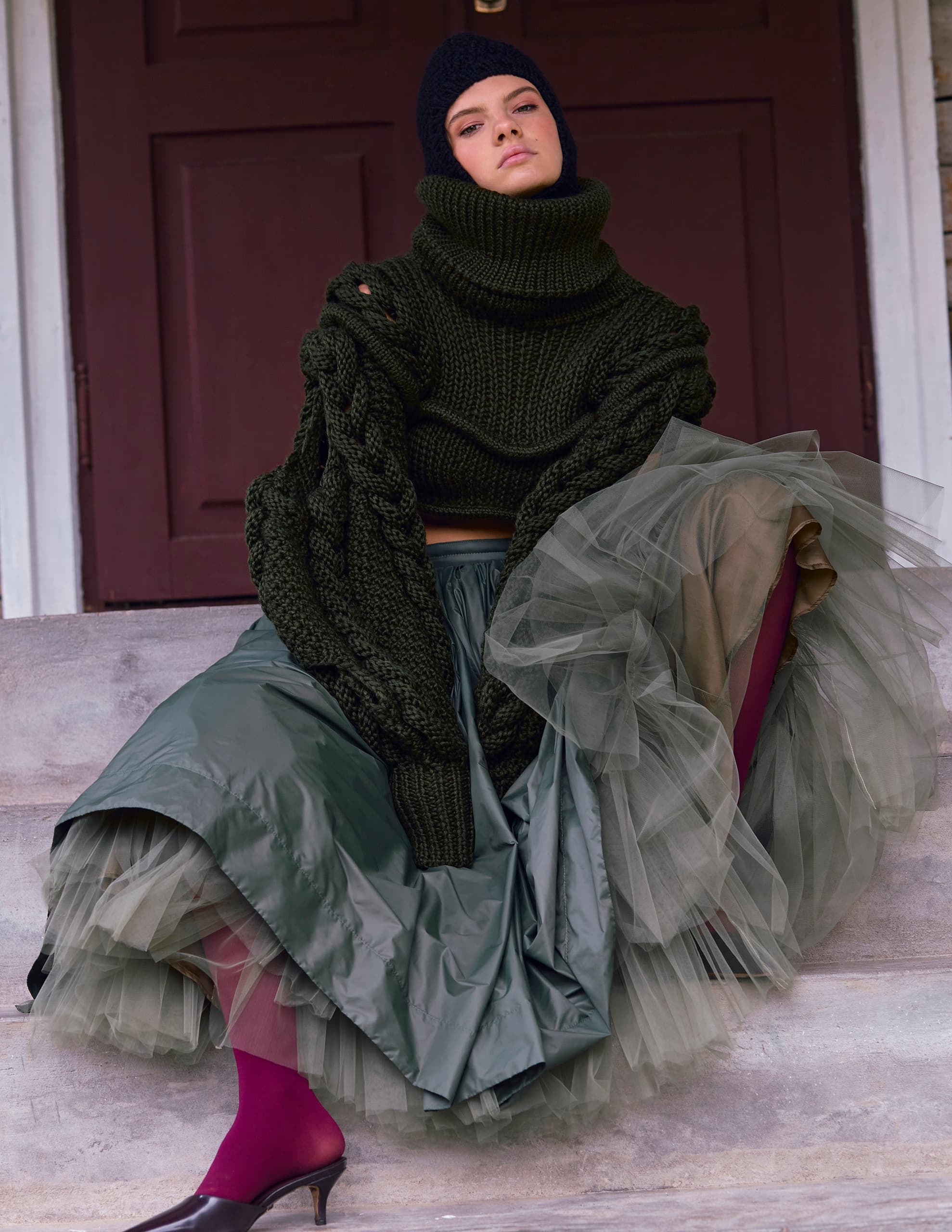 Fashionable woman in layered green outfit sitting on steps.