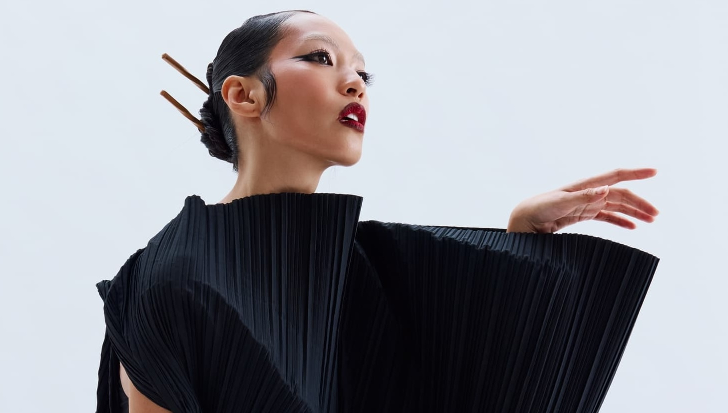 Elegant woman in black pleated dress with artistic pose against white backdrop.