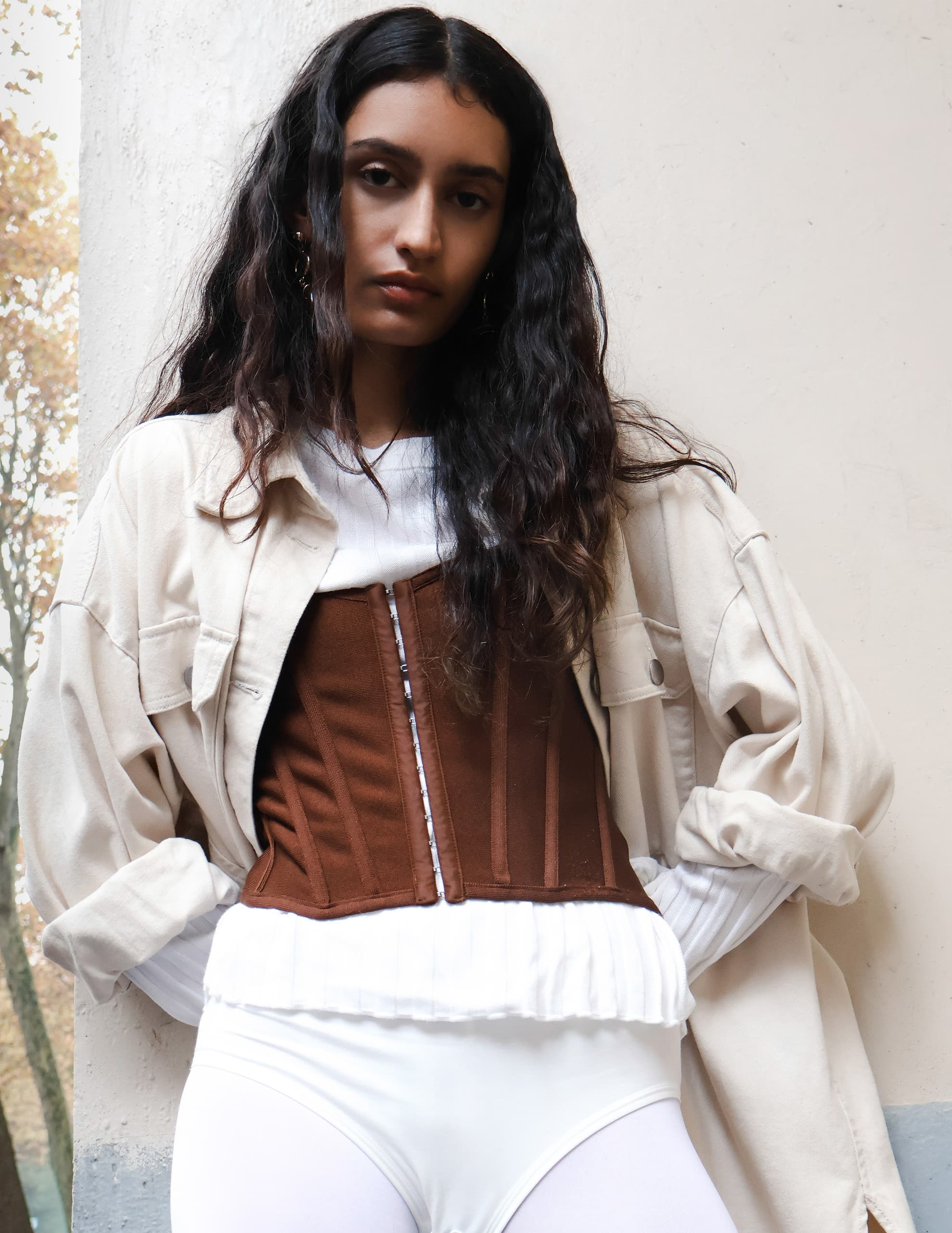 Woman in layered fashion with corset and oversized jacket stands confidently.