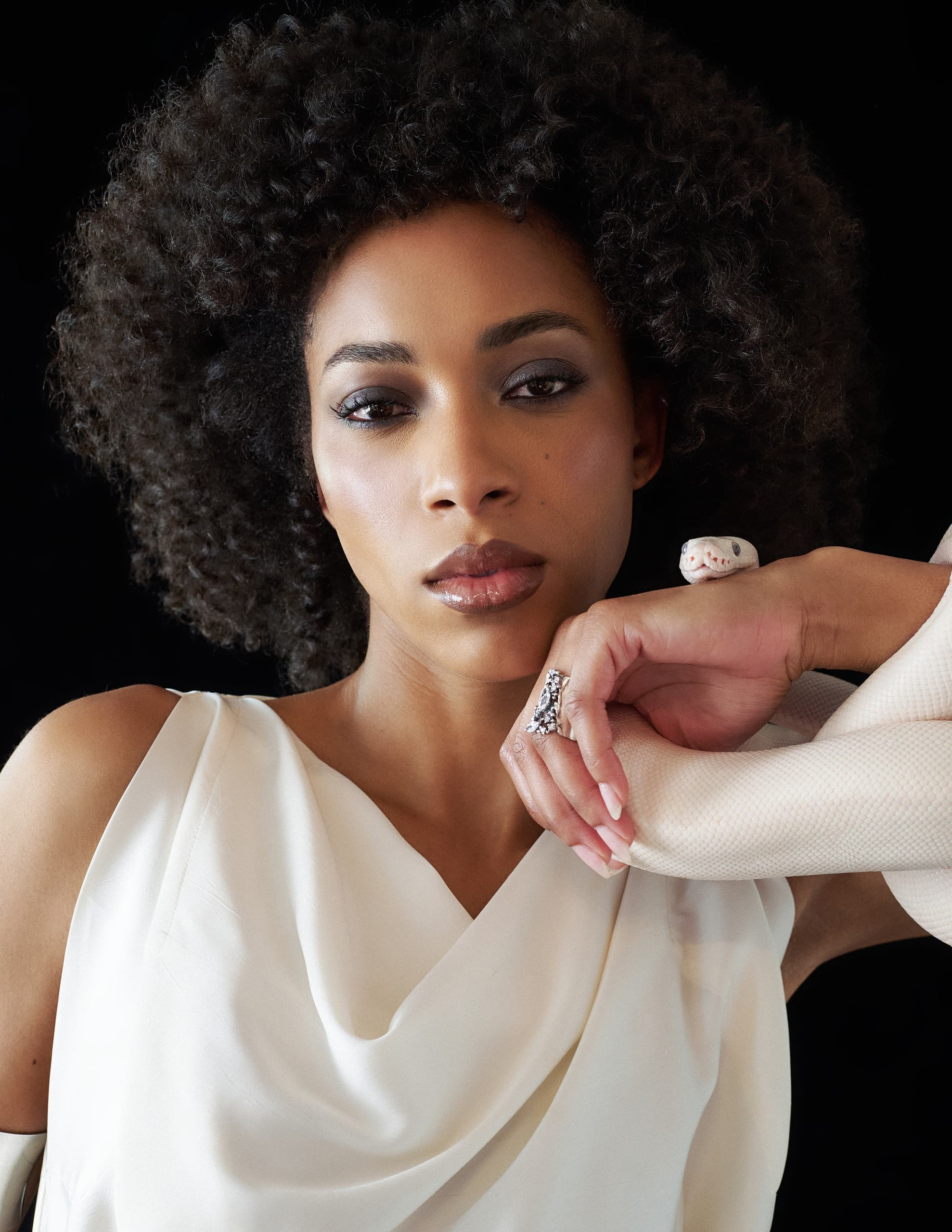 Woman with curly hair and a snake accessory, wearing white outfit.