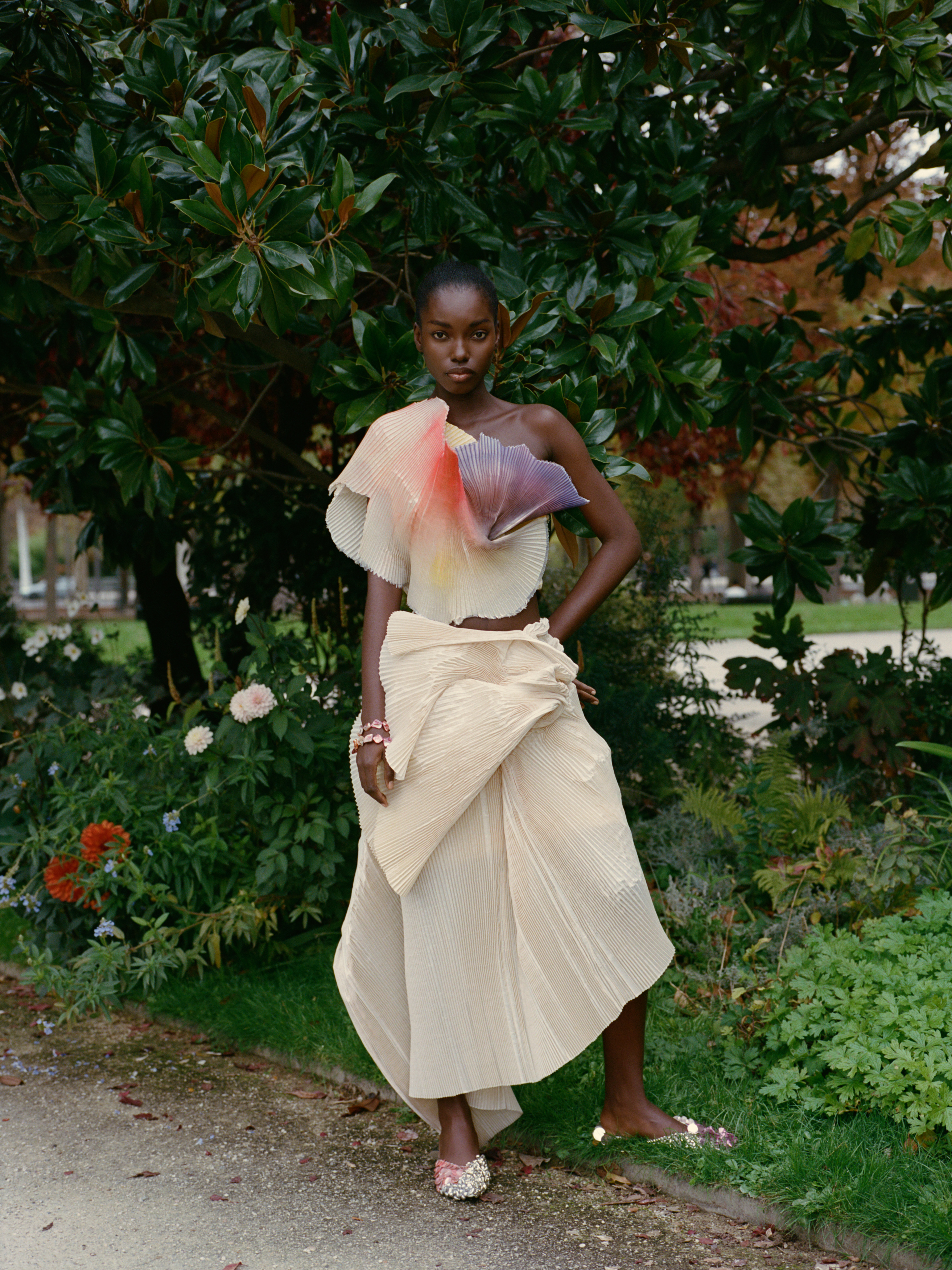 Fashion model in an artistic outfit standing in a garden setting.