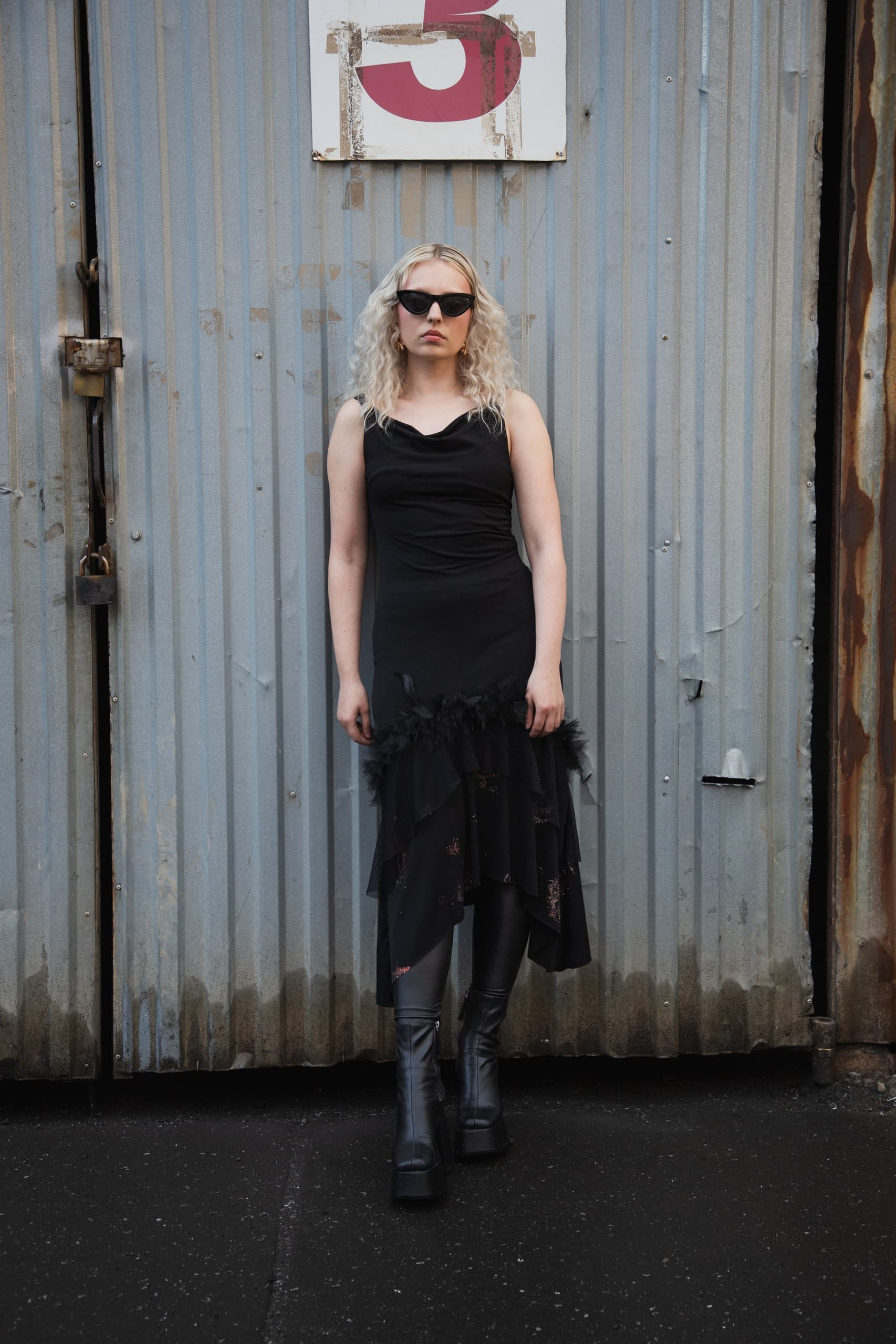 Woman in black dress and boots near industrial door.