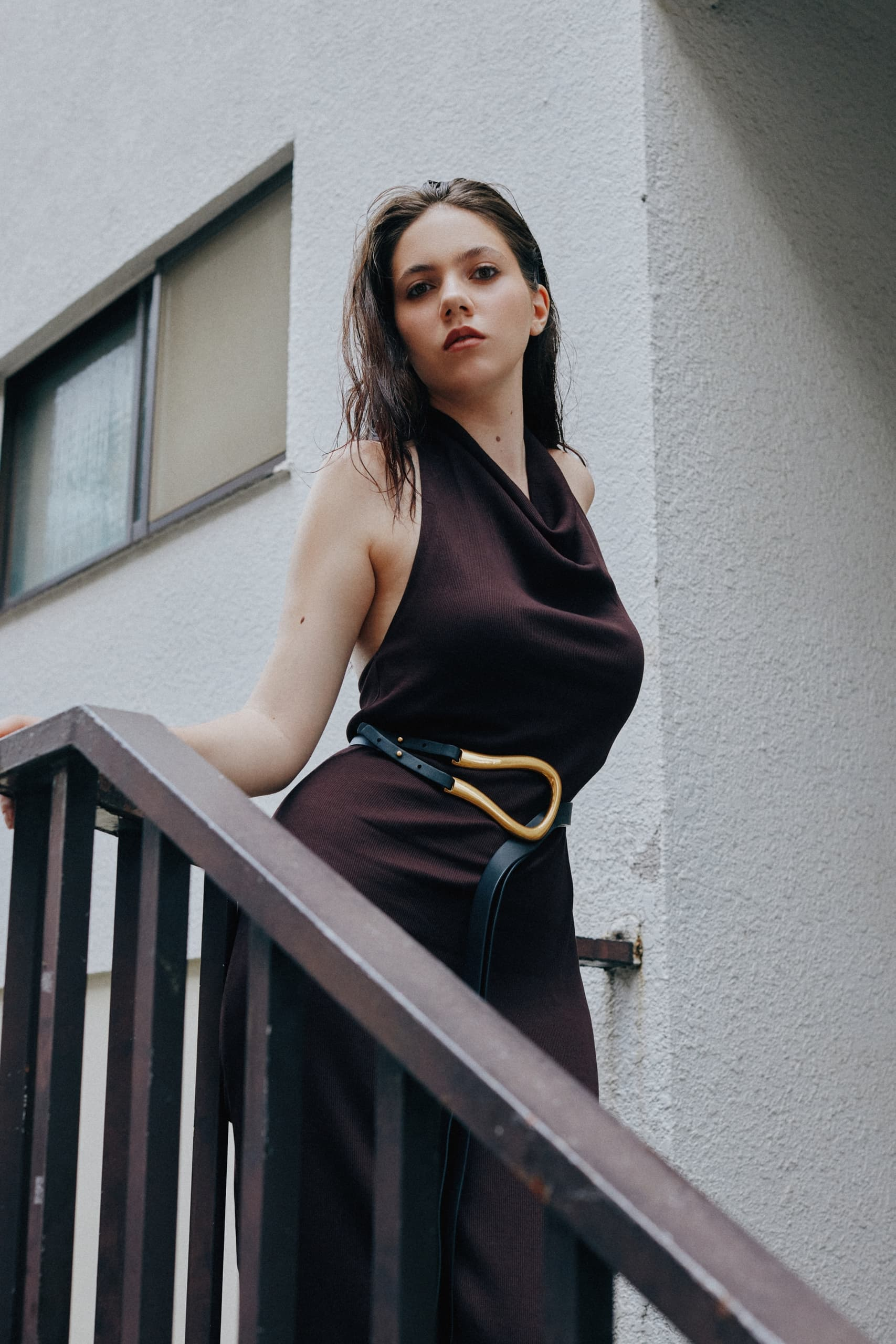 Woman in stylish brown dress stands on staircase, urban background.