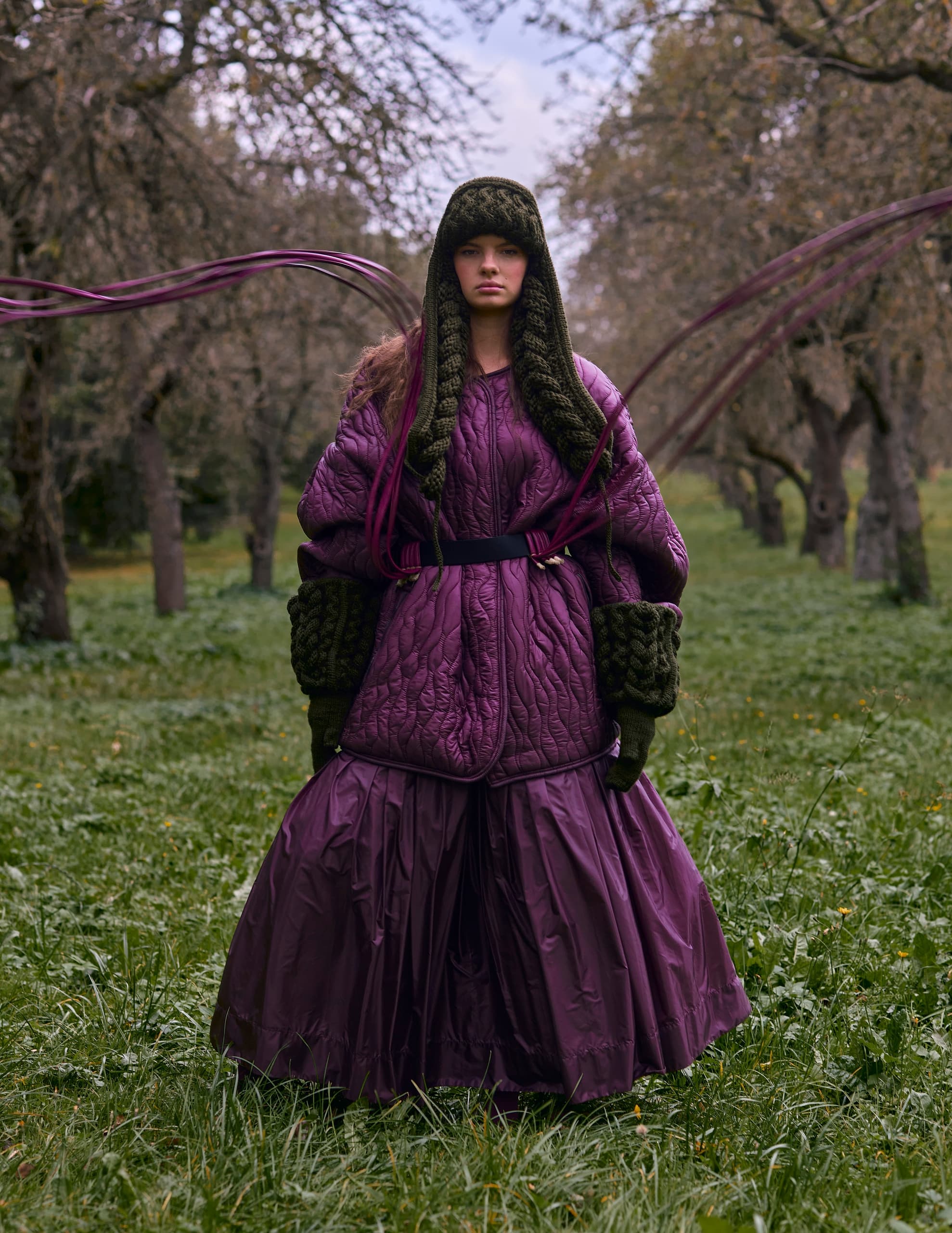 Woman in a purple quilted outfit in a scenic, tree-filled landscape.