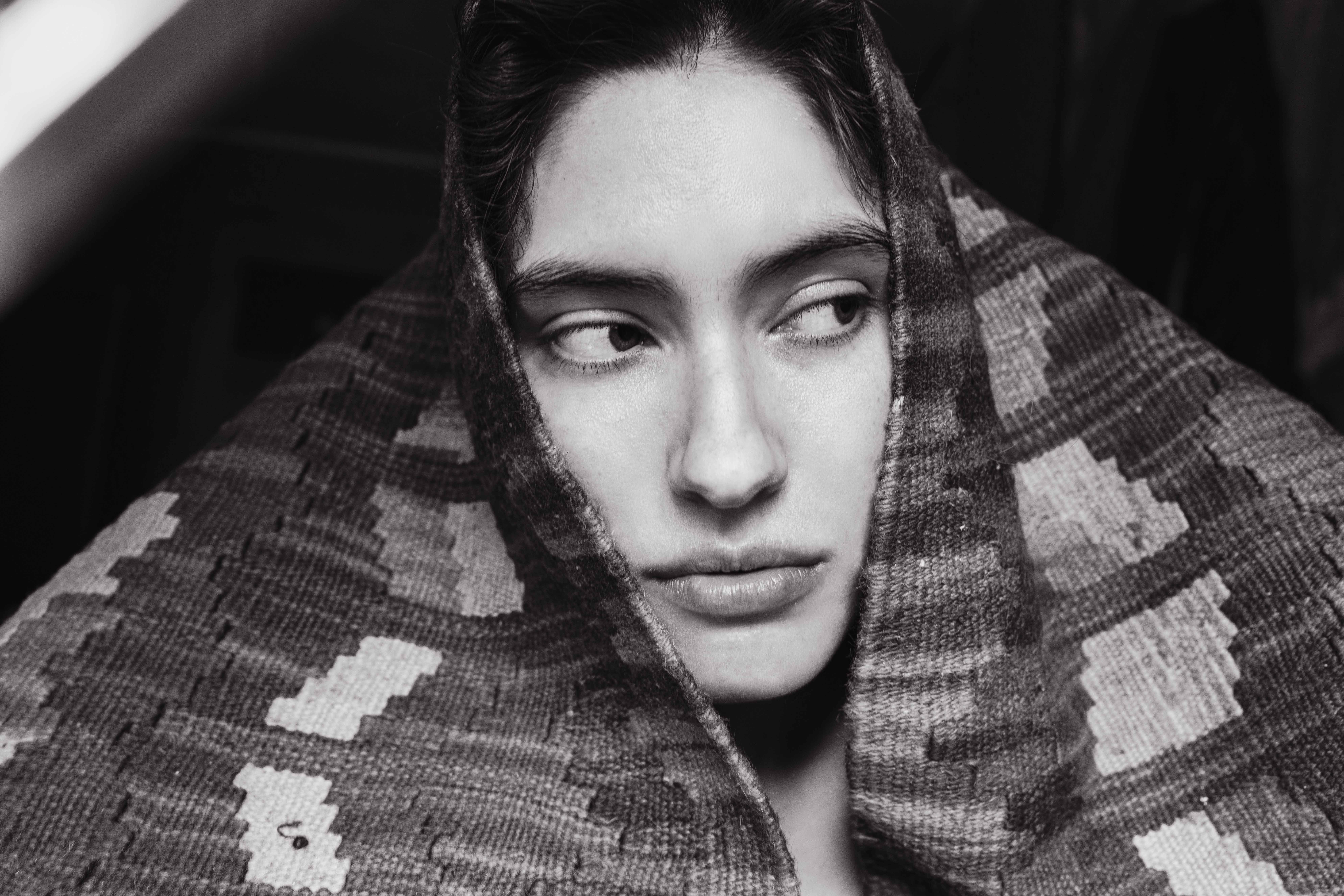 Person wrapped in patterned fabric looking sideways, black and white portrait.