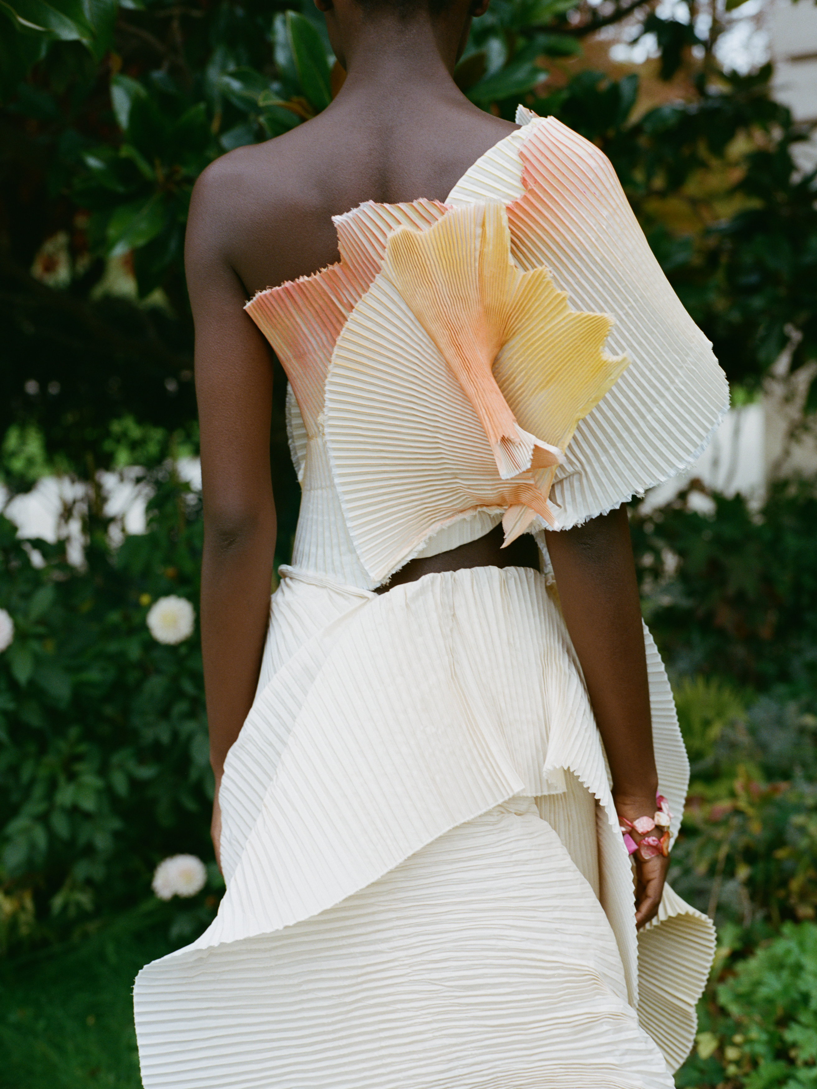 Elegant pleated dress with colorful ruffles in a garden setting.