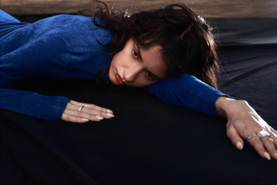 Person in blue outfit lying on a black surface, looking thoughtful and introspective.
