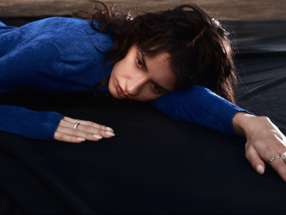 Person in blue outfit lying on a black surface, looking thoughtful and introspective.