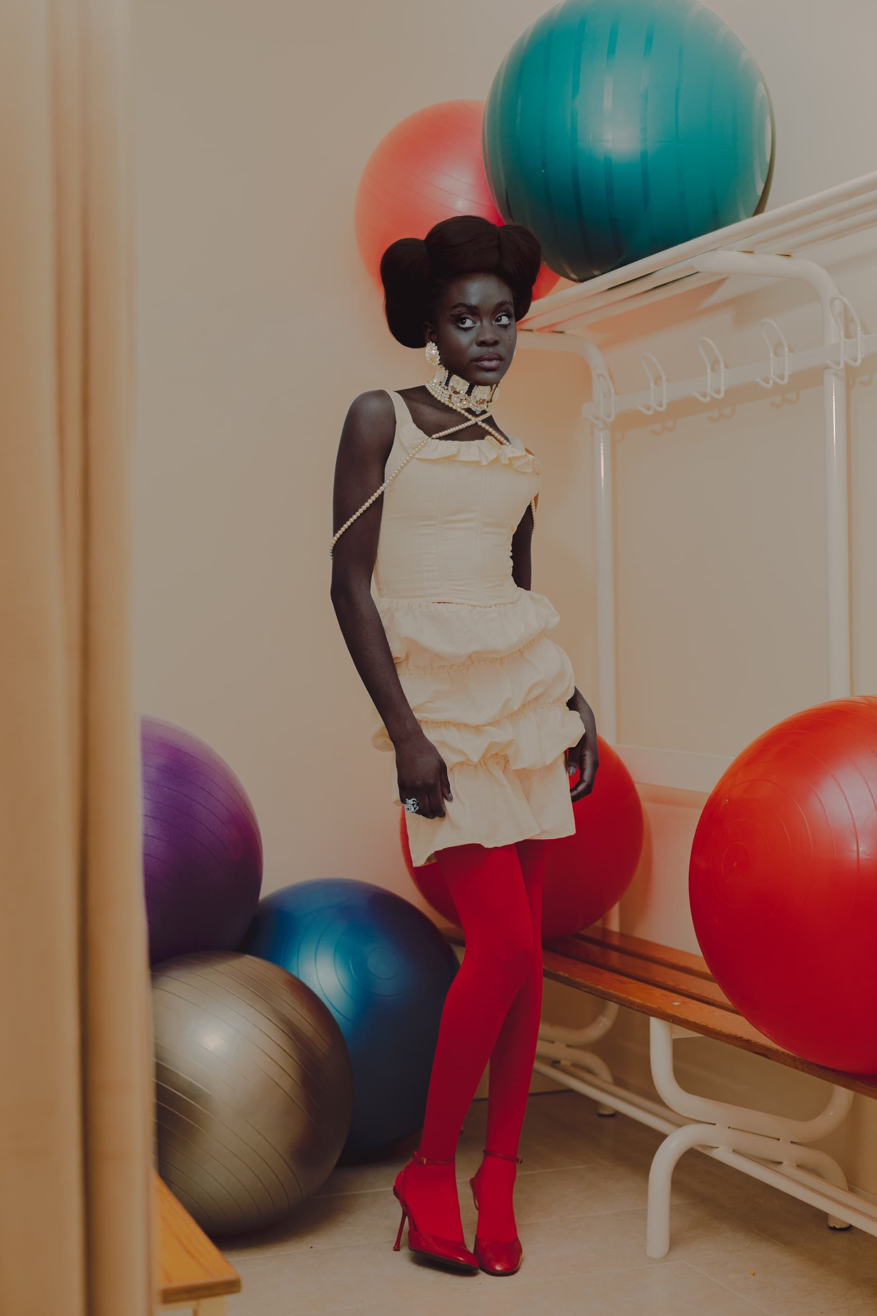 Fashionable woman in red tights and heels, posing by colorful exercise balls.