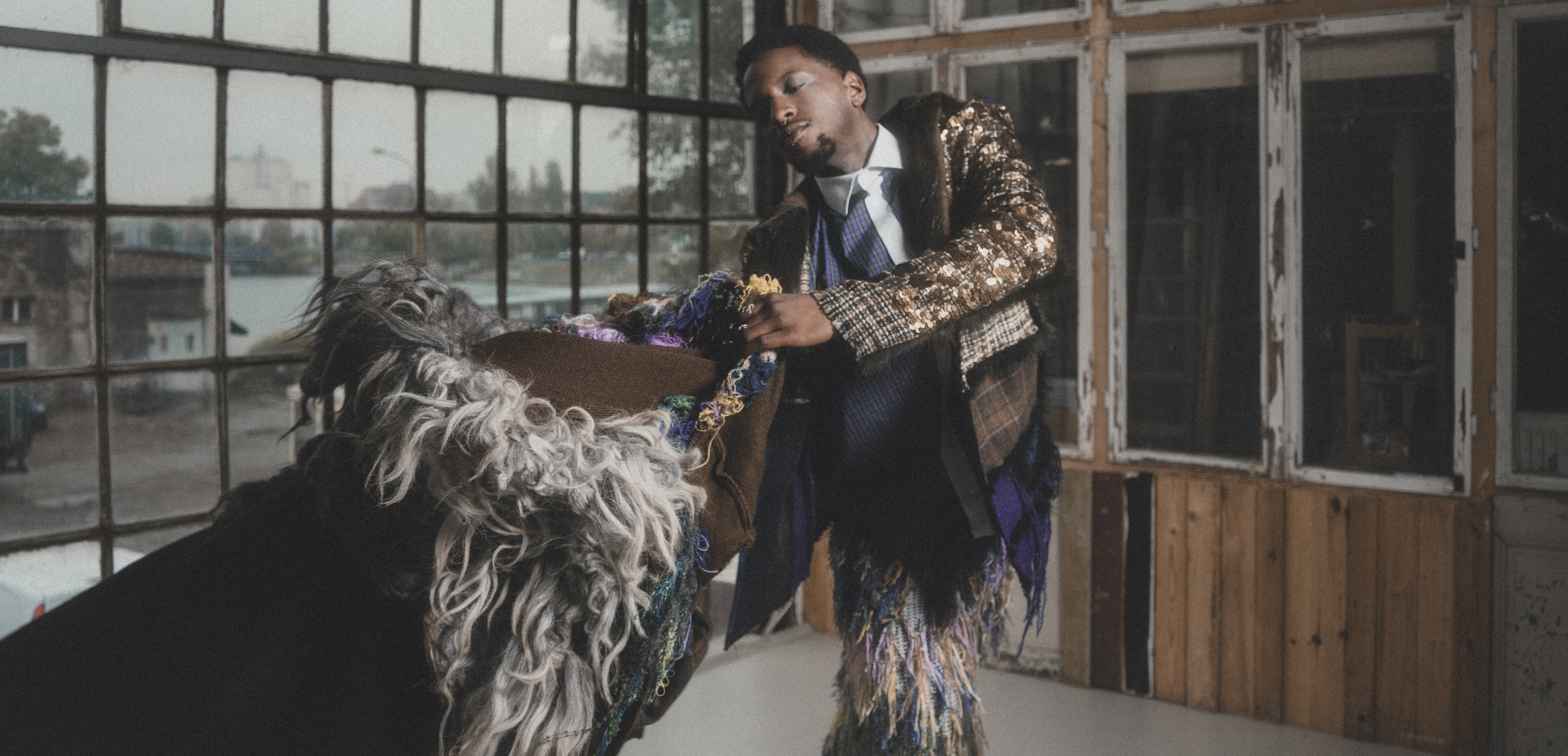 Person in vibrant, eclectic fashion posing indoors near large windows.