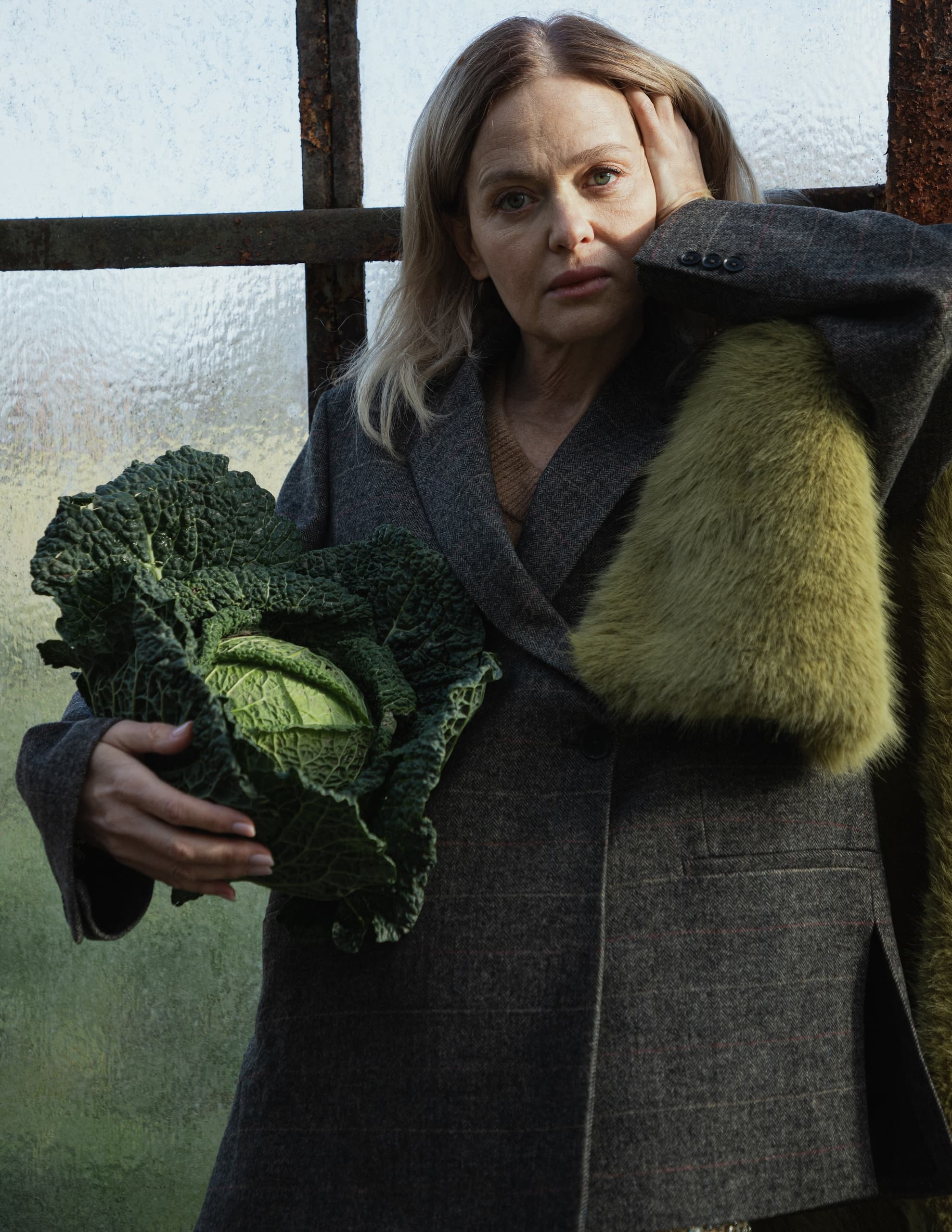 Woman in a coat holding a large leafy cabbage in natural light.