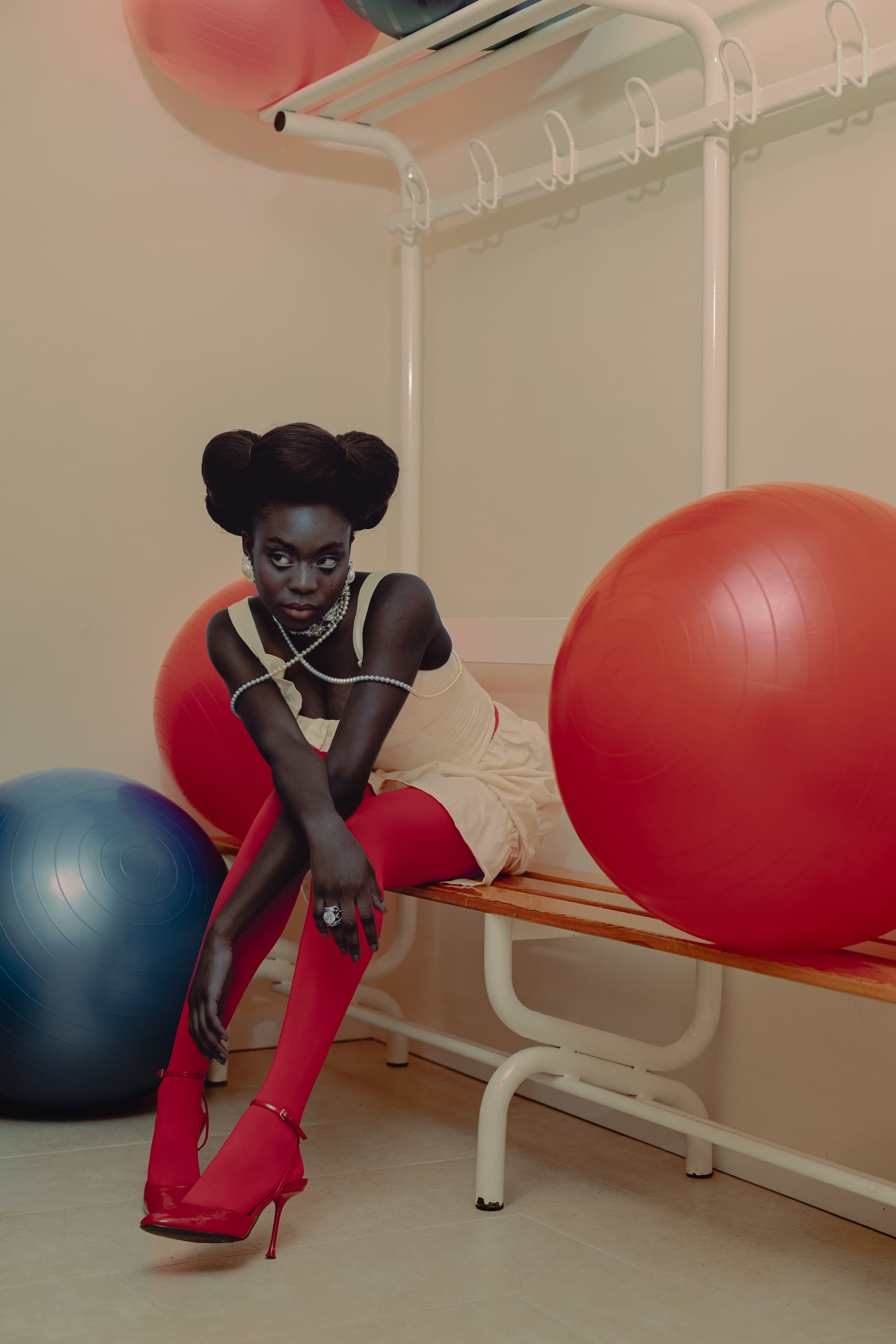 Fashionable woman in red tights seated near exercise balls in gym.