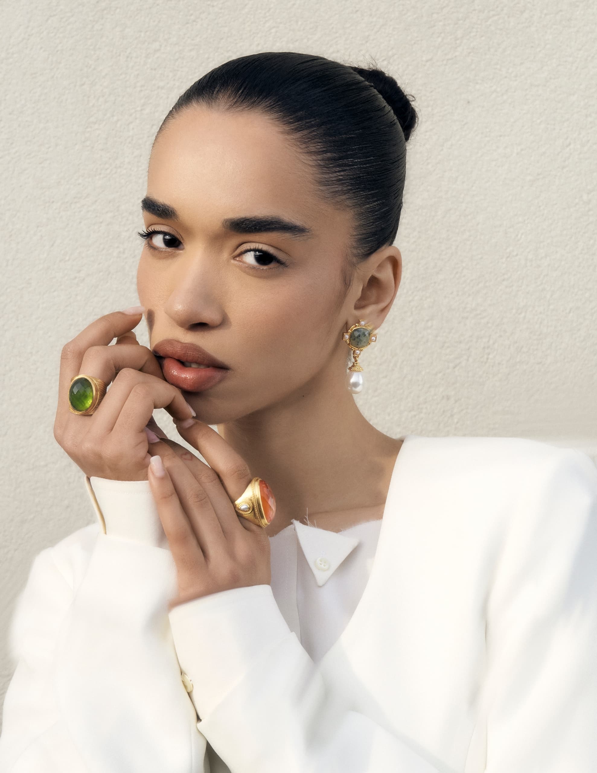 Elegant woman wearing gold jewelry, pearl earrings, and a white outfit.