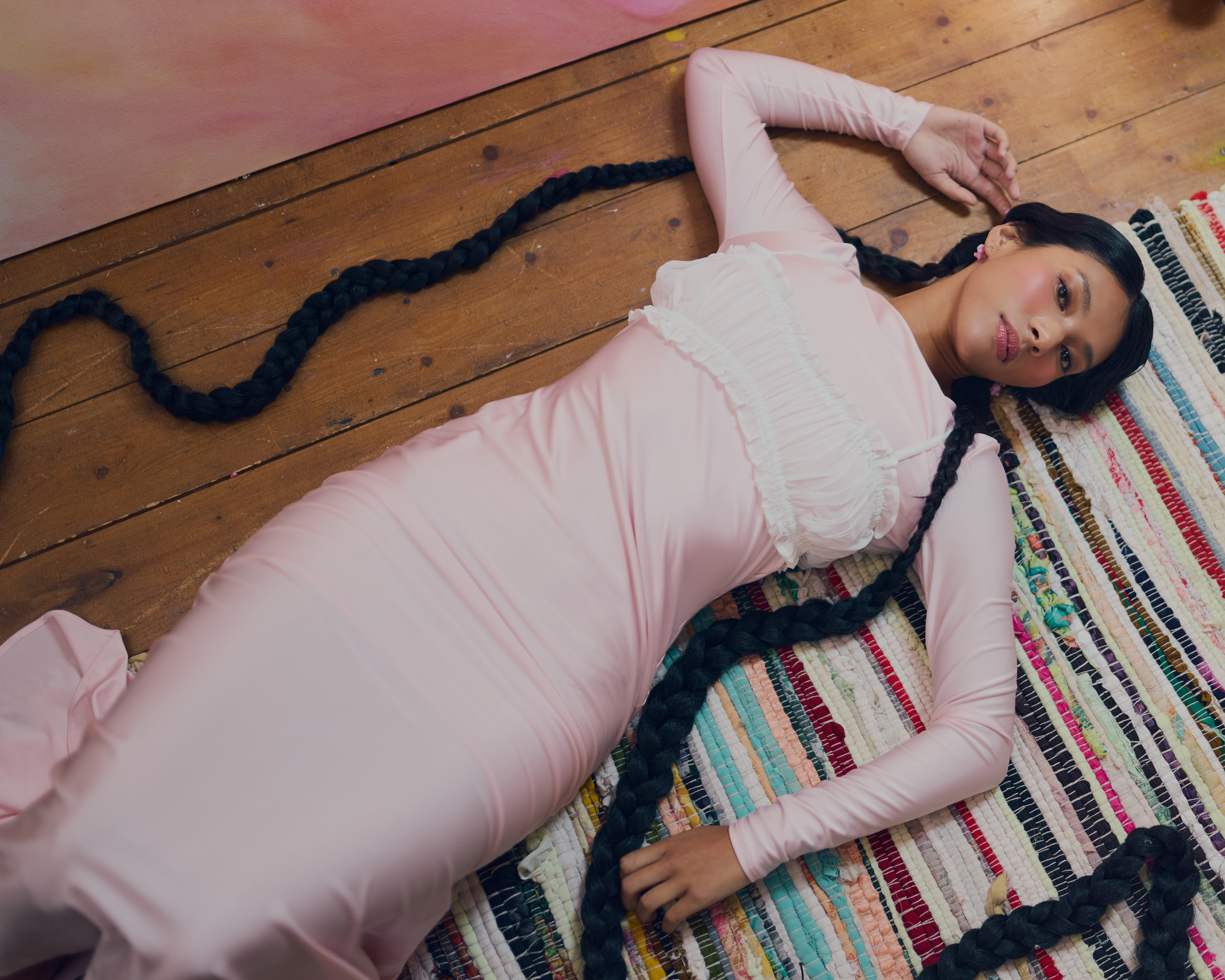 Woman in pink dress with braided hair lying on colorful striped rug.