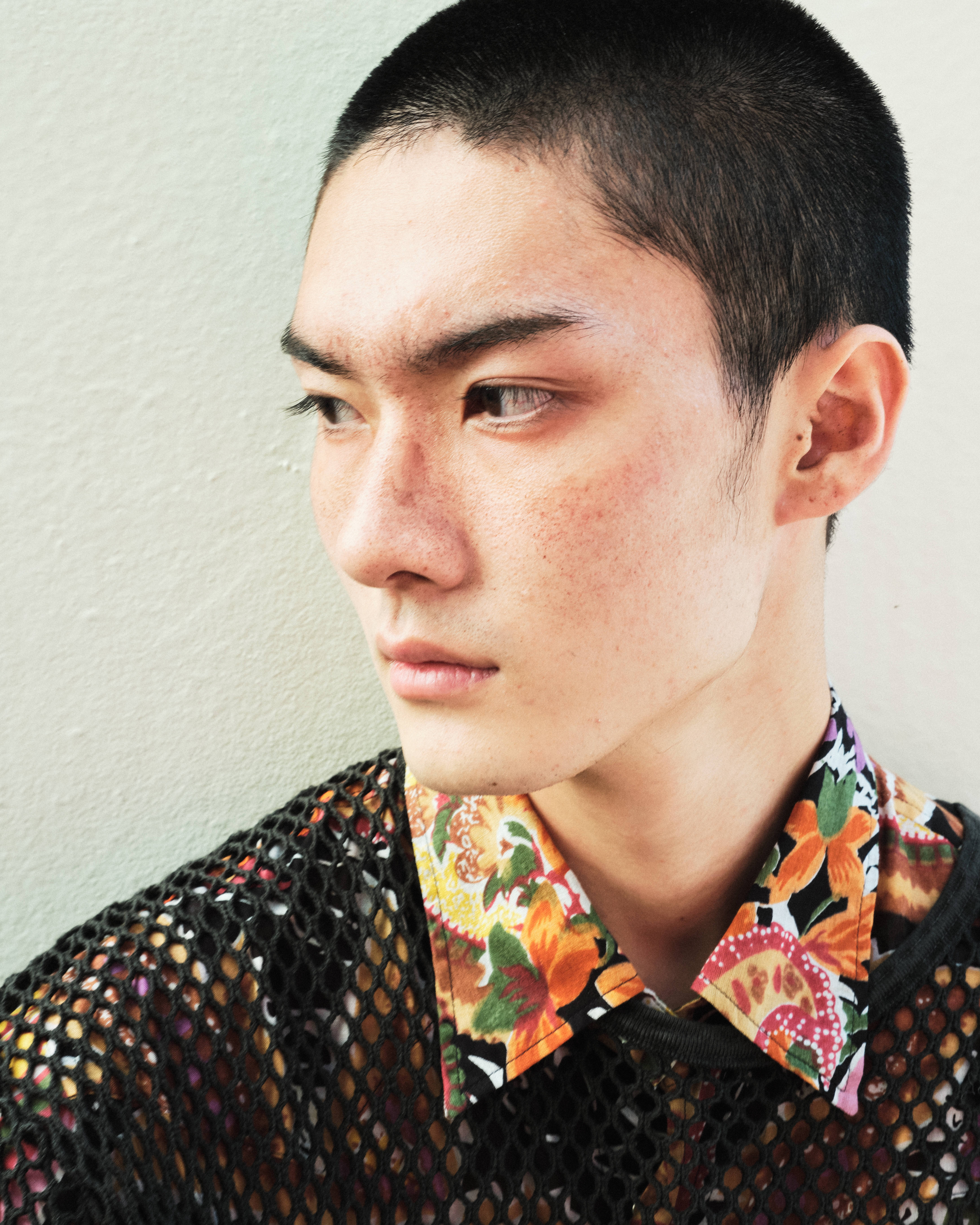 Person in floral shirt with black mesh overlay gazing to the side.