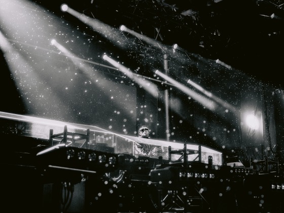 DJ performing in a dramatic stage setting with spotlights and atmospheric effects.