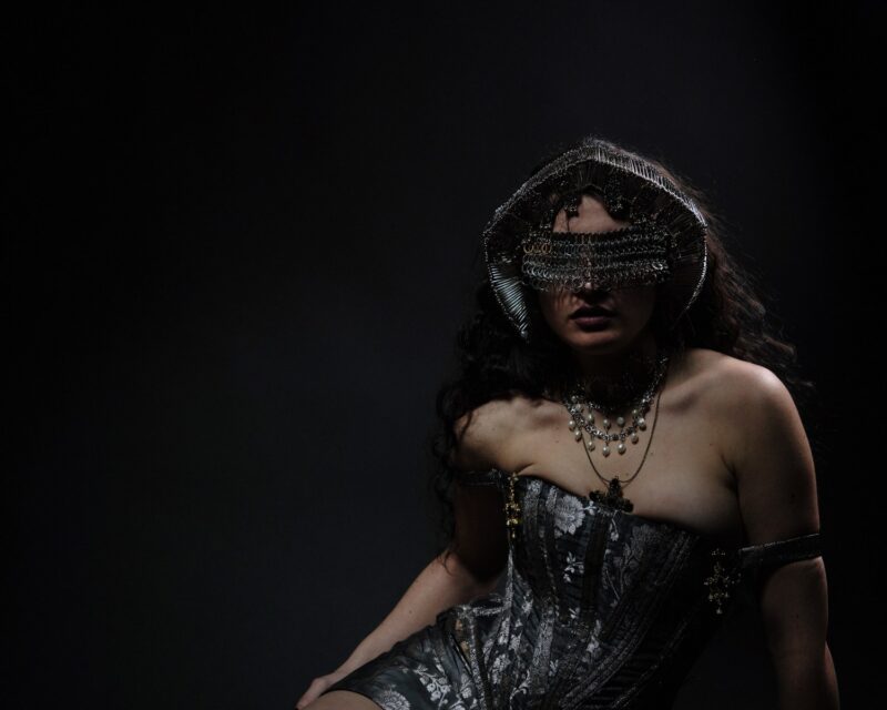 Mysterious woman in gothic attire with chain headdress and dramatic lighting.