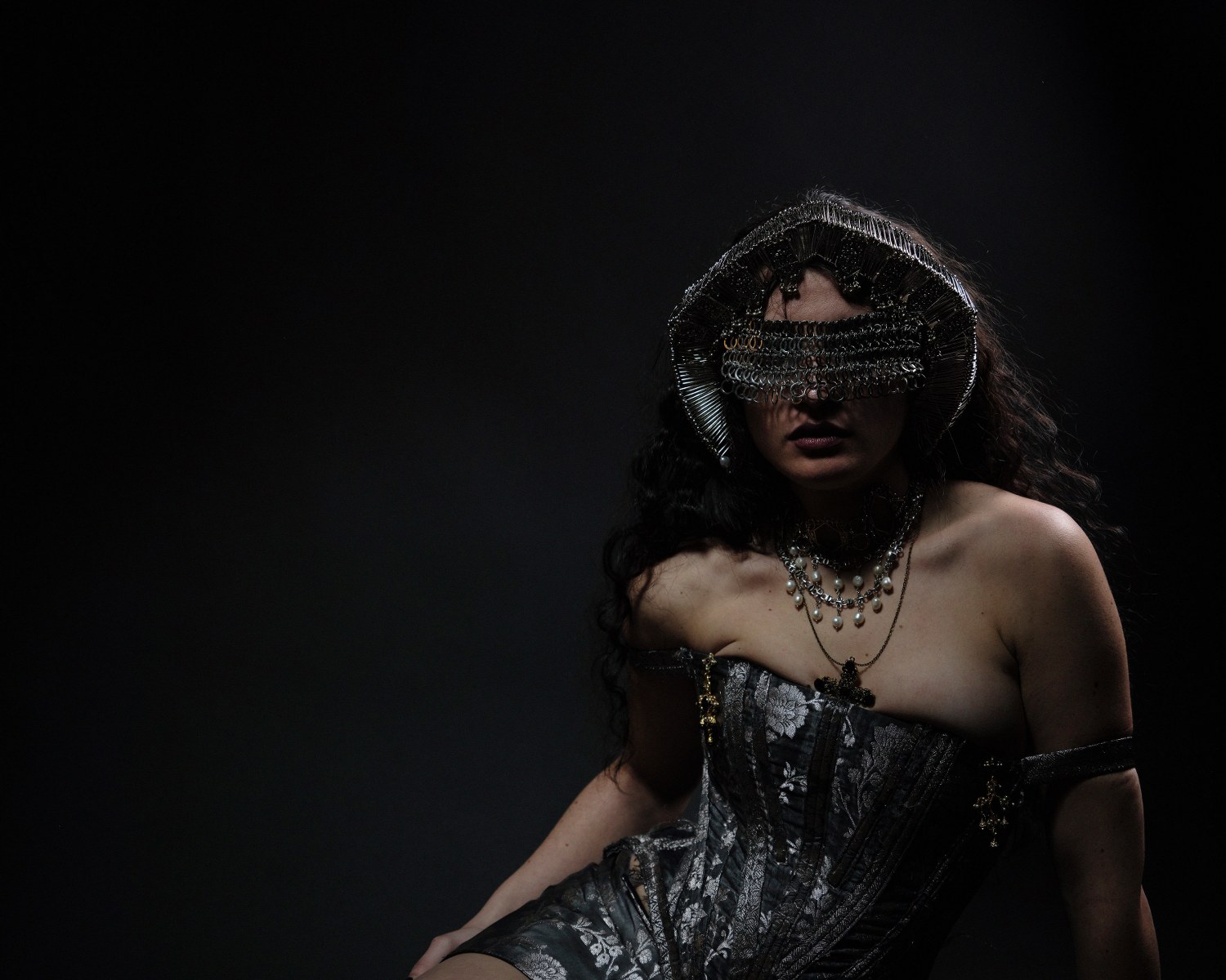 Mysterious woman in gothic attire with chain headdress and dramatic lighting.