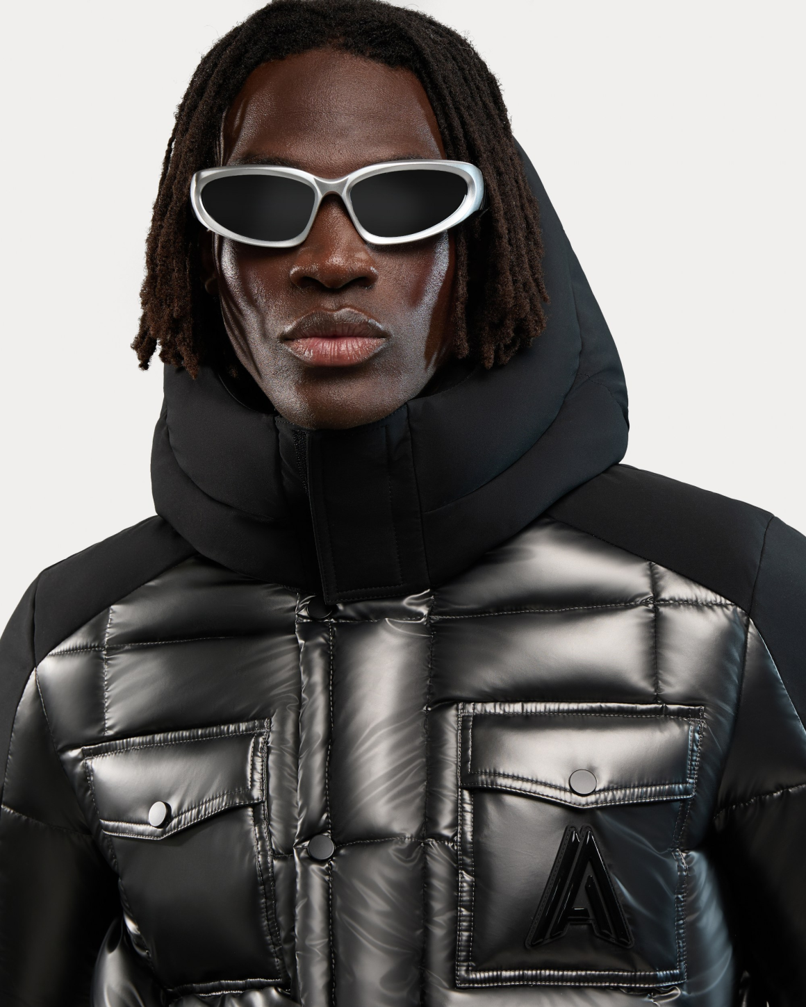 Man in sleek black puffer jacket and futuristic sunglasses against a white background.
