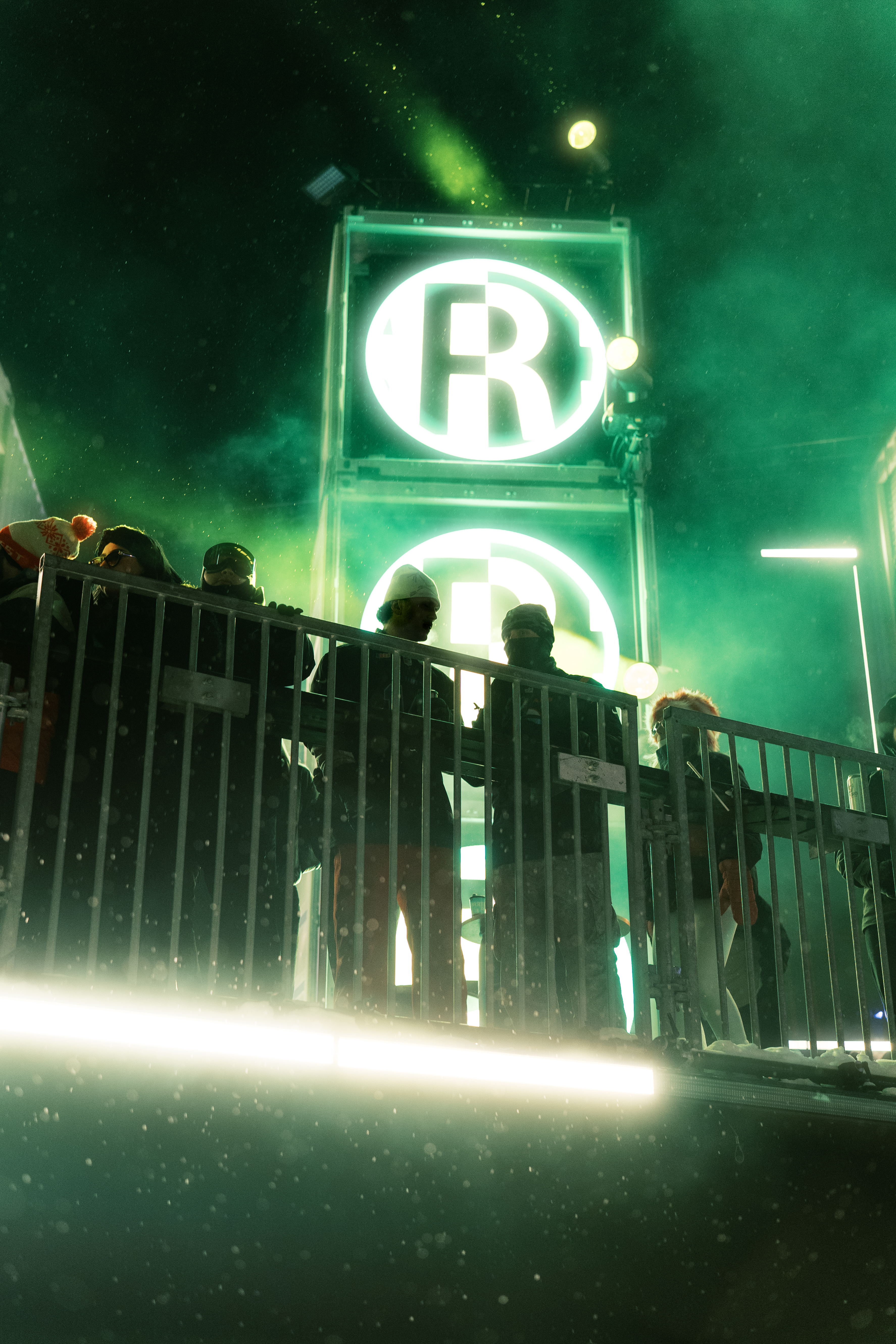 Crowd under neon lights with R signs at a night event.