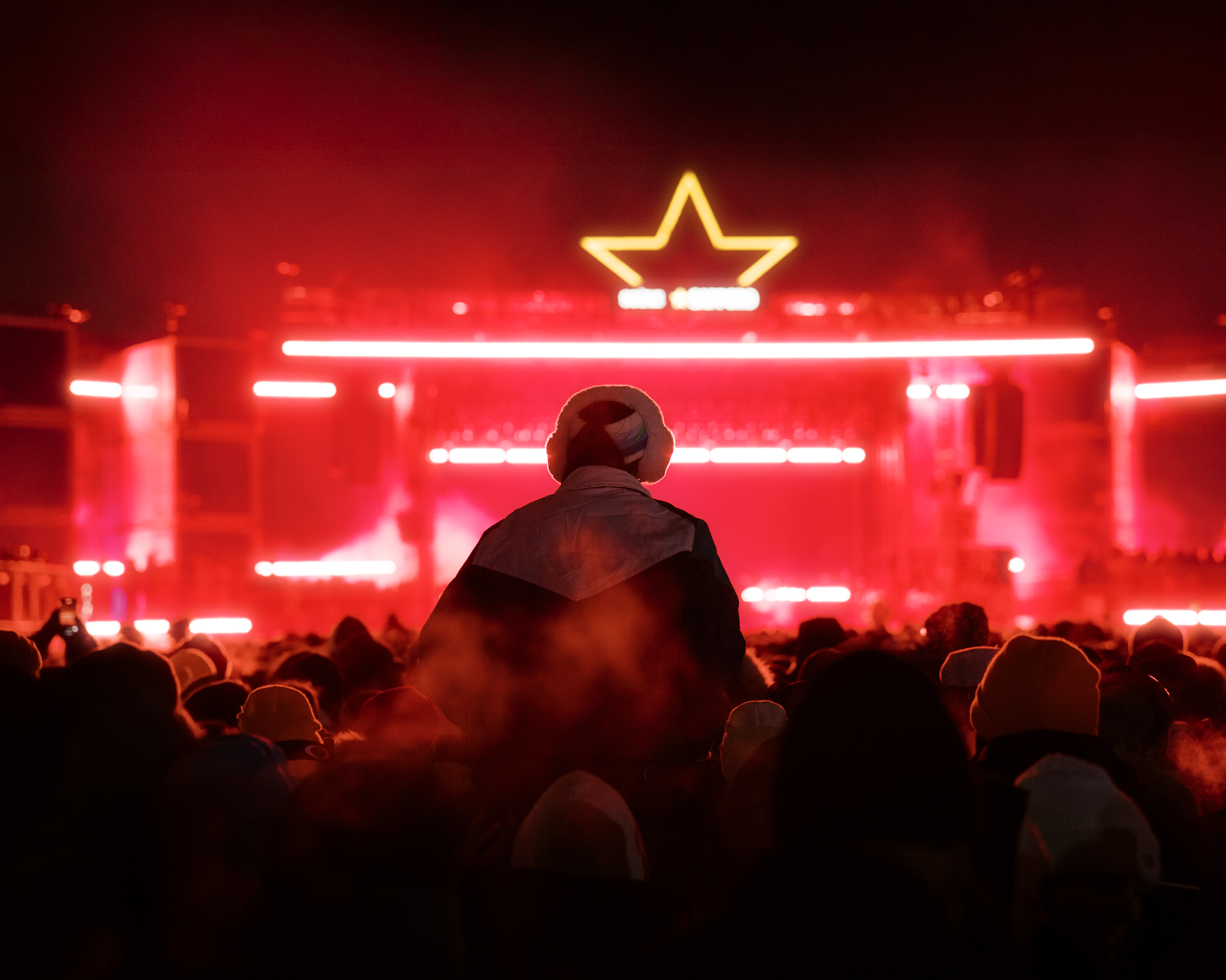 Crowd enjoys nighttime concert with vibrant red lights and a star-shaped stage design.