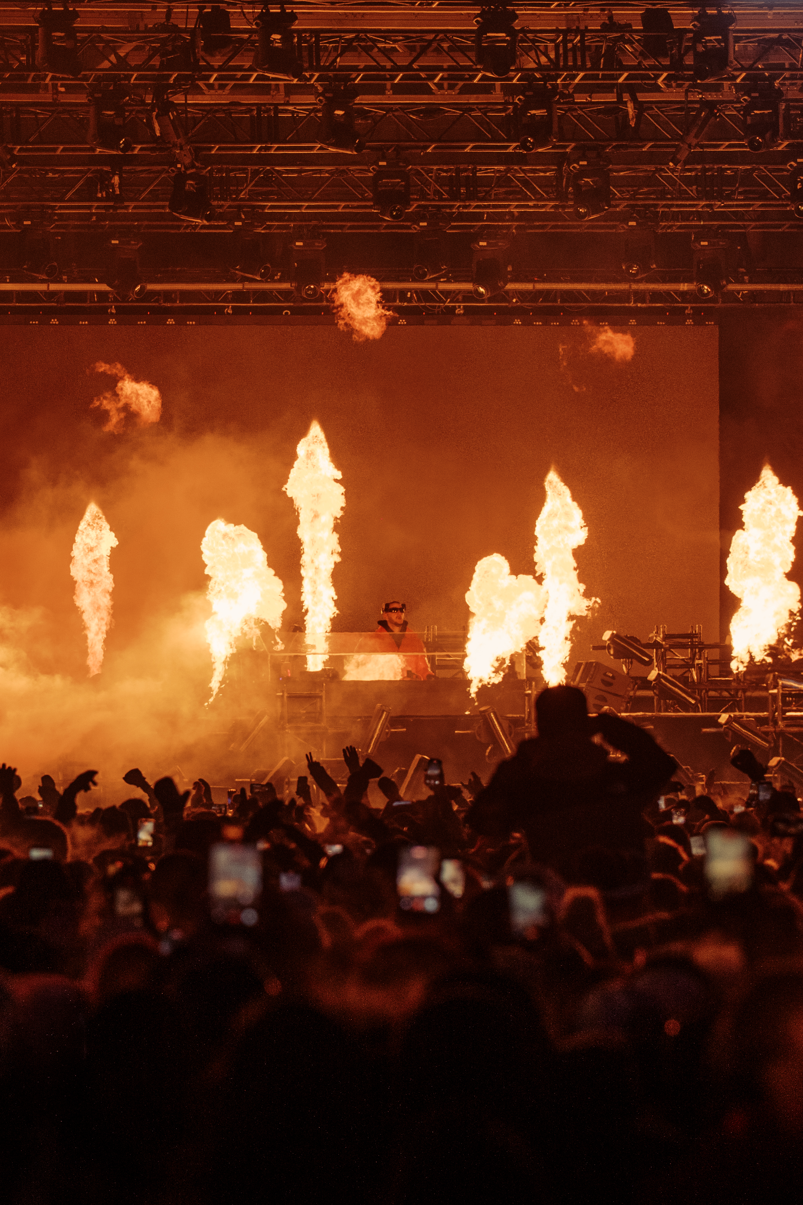 DJ performing with fire effects at a lively concert stage.