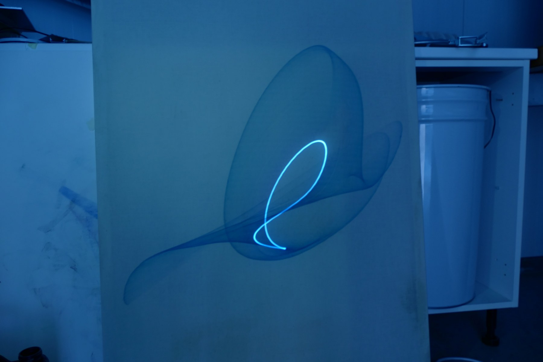 Abstract blue light swirl on a canvas in a dimly lit room.