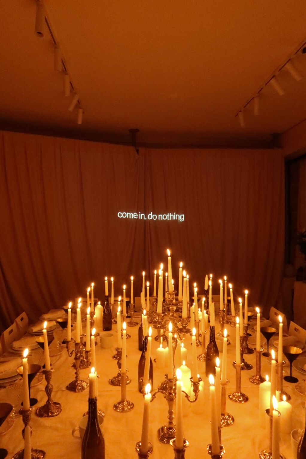 Candlelit table with come in, do nothing text on wall for a cozy ambiance.