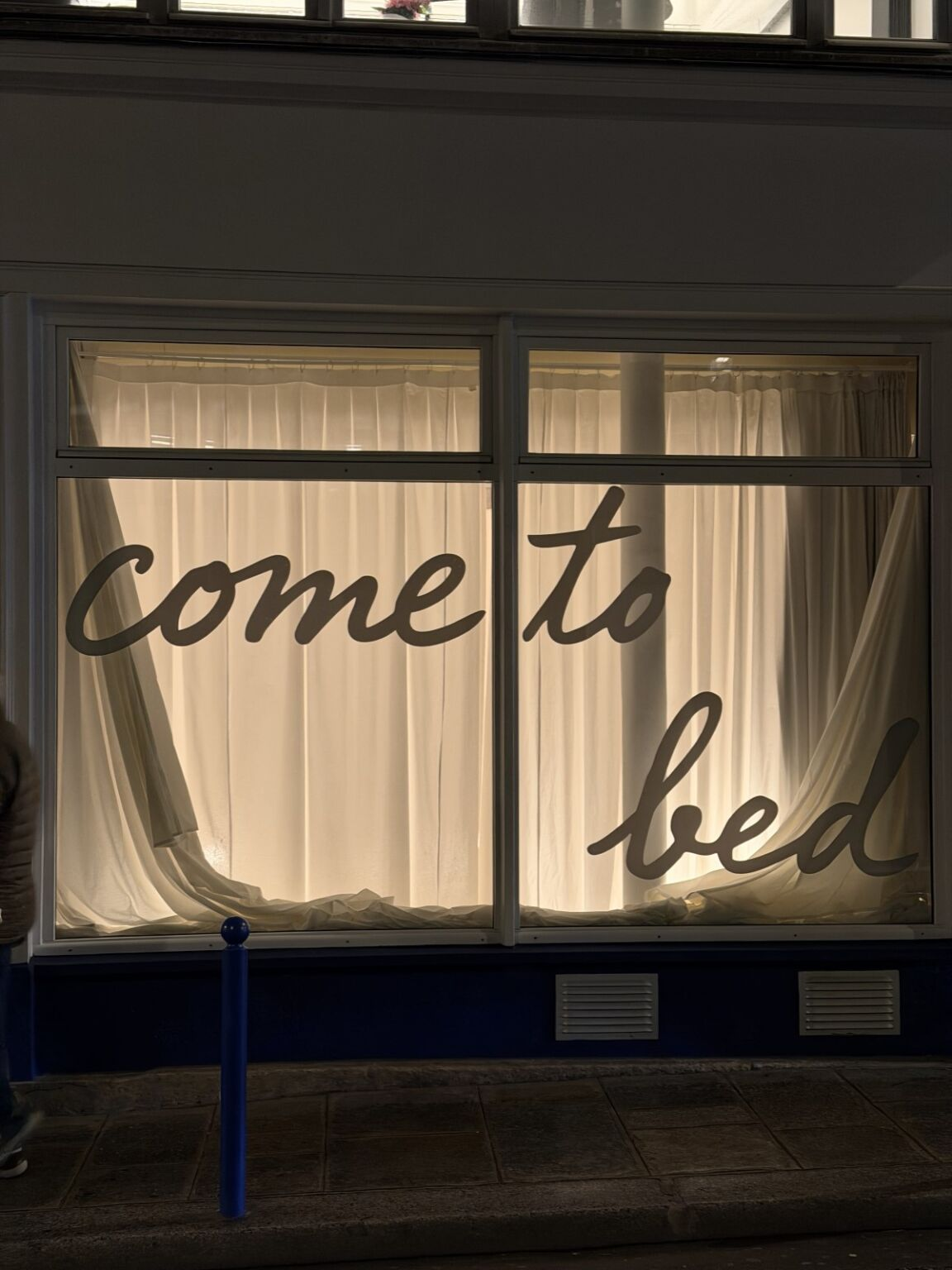 Storefront with come to bed text on window, night view with curtains drawn.