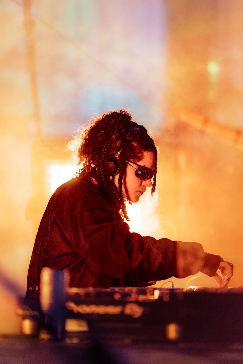 DJ performs live set with vibrant orange background.