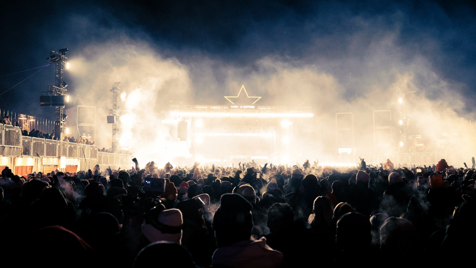 Crowd enjoying a vibrant outdoor concert at night under bright stage lights.