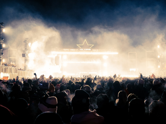 Crowd enjoying a vibrant outdoor concert at night under bright stage lights.