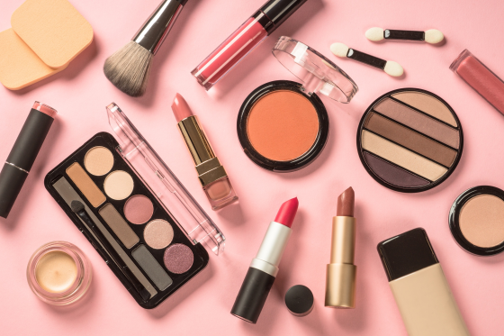 Assorted makeup items on a pink background, including lipsticks and eyeshadow palettes.
