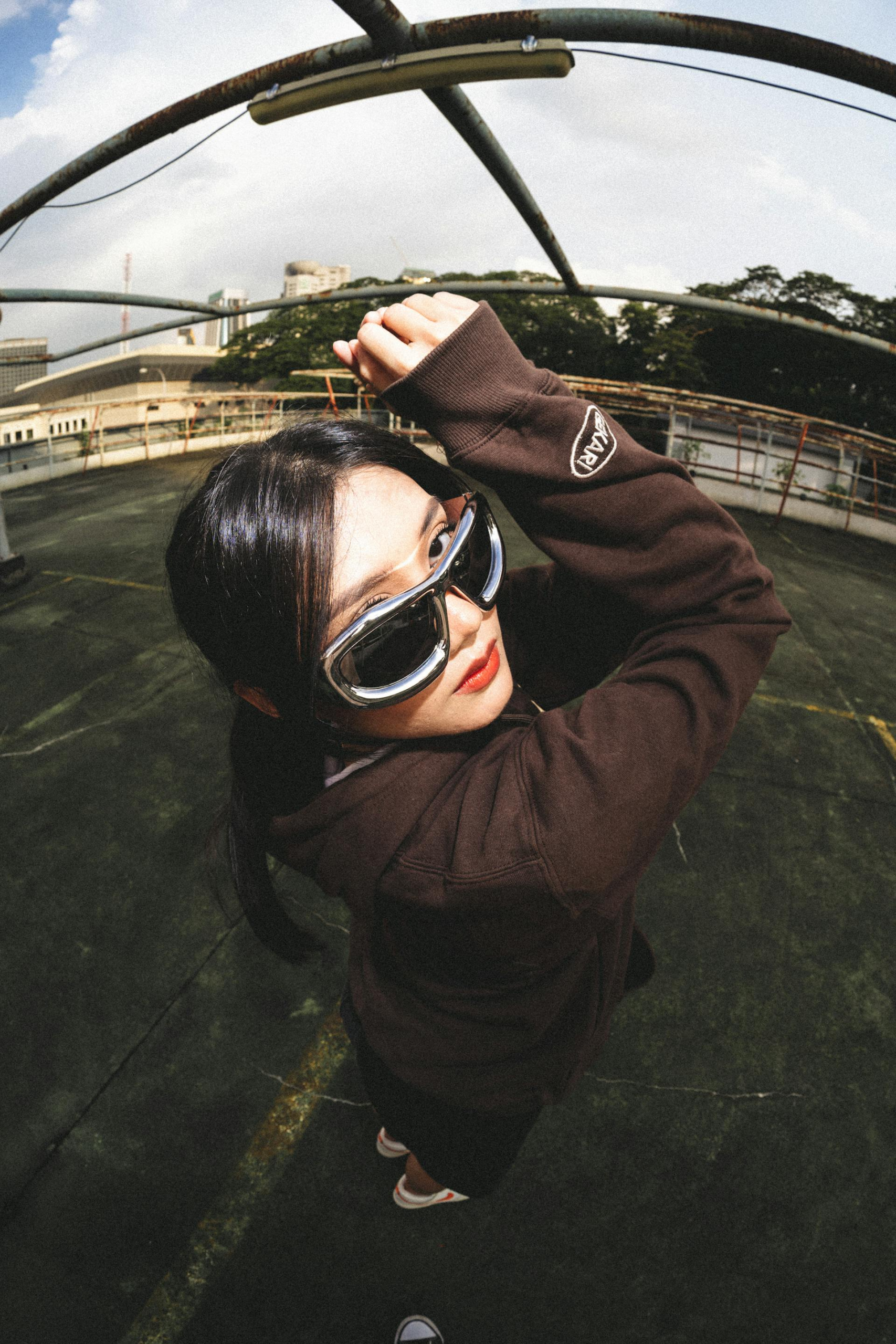 Person in sunglasses and brown jacket on rooftop, striking a confident pose.