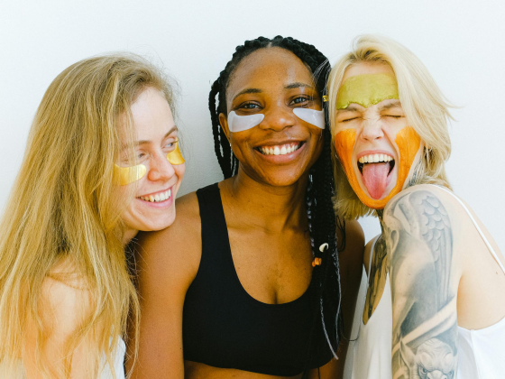 Three women smiling with colorful face masks and under-eye patches.