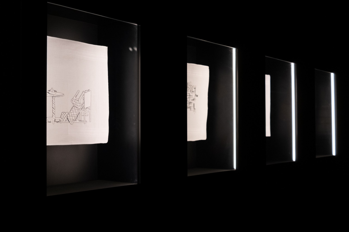 Artwork display in dark exhibit with illuminated white canvases featuring minimal sketches.