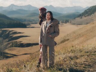 Two people in stylish outfits stand in a picturesque mountain landscape.