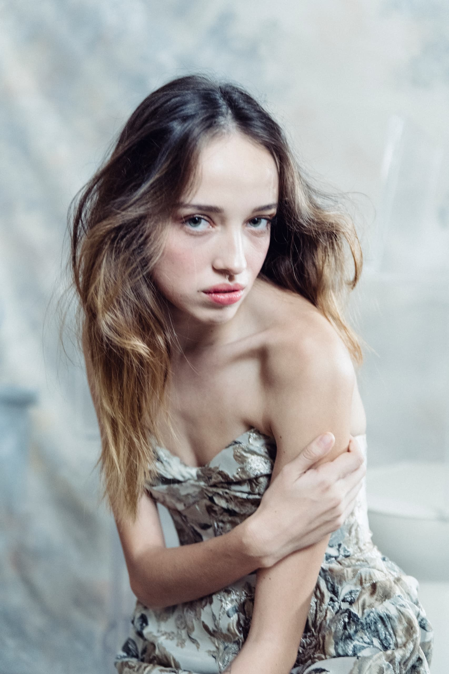 Woman in elegant floral dress with soft lighting, looking thoughtfully at the camera.